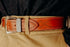 Close-up of brown leather belt with metal studs and engraved silver buckle worn with tan pants and dark denim shirt