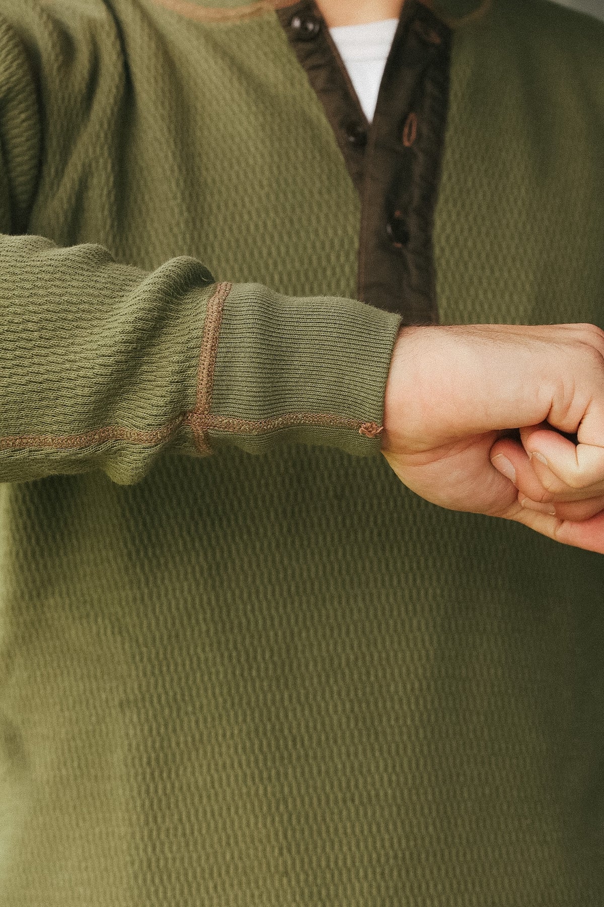 Close-up of a person wearing an olive green textured henley shirt with a dark brown button placket and contrast stitching.