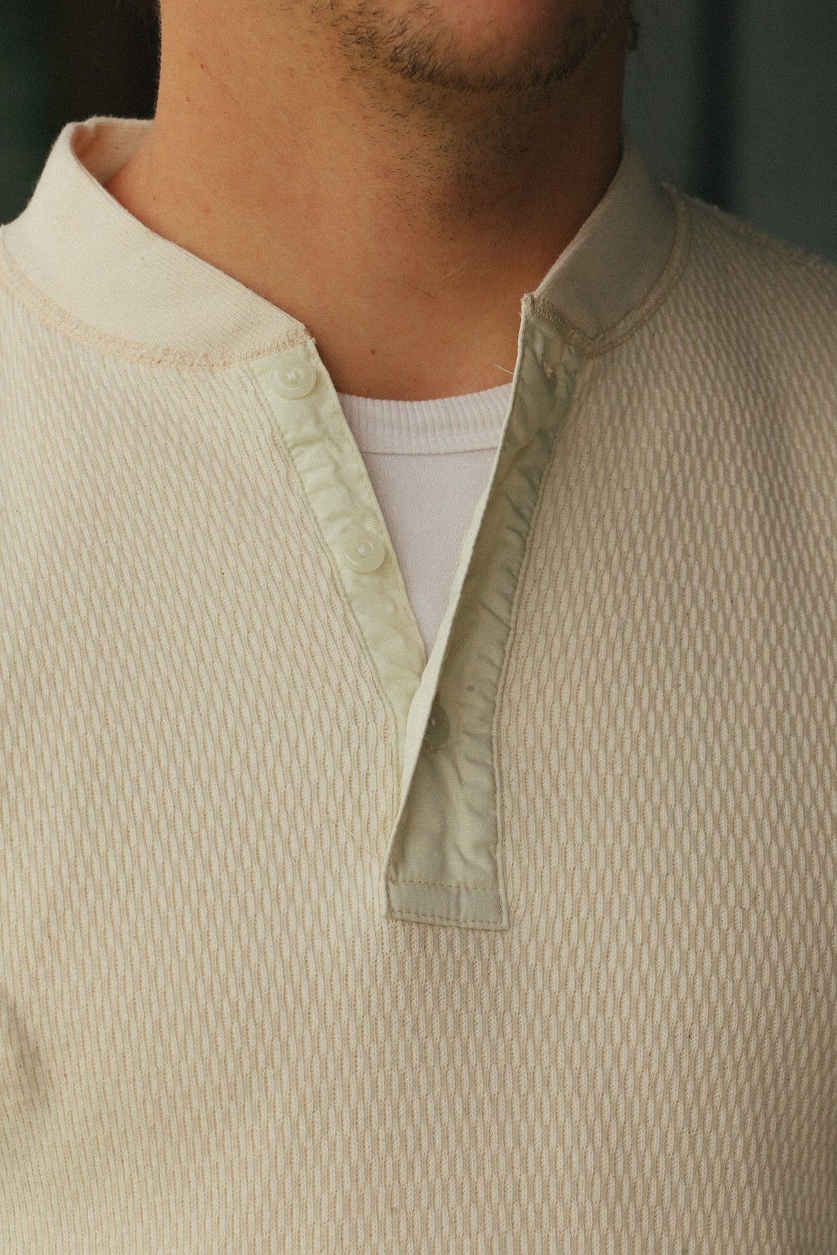 Close-up of a man wearing a textured cream-colored henley shirt with a buttoned collar over a white undershirt.