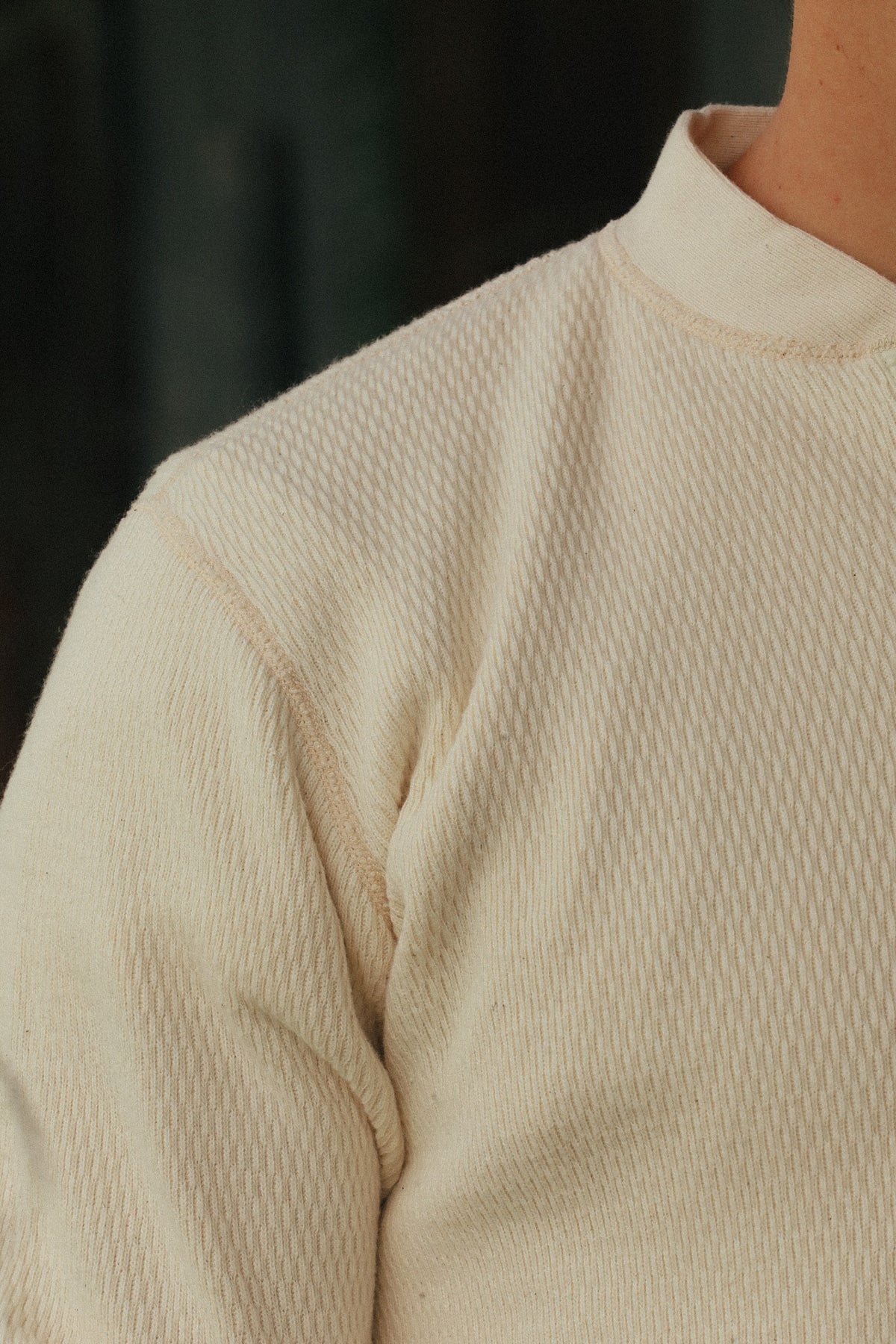 Close-up of a person wearing a cream-colored textured knit top with a mock neck collar.
