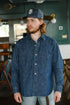 Man wearing navy blue denim shirt and dark baseball cap indoors in casual setting