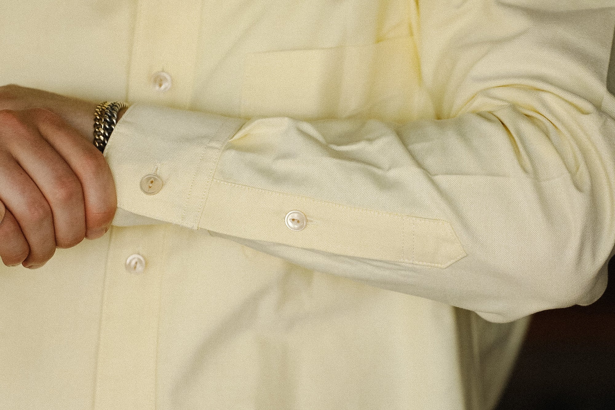 Close-up of a light-colored shirt with buttons and rolled-up sleeve.