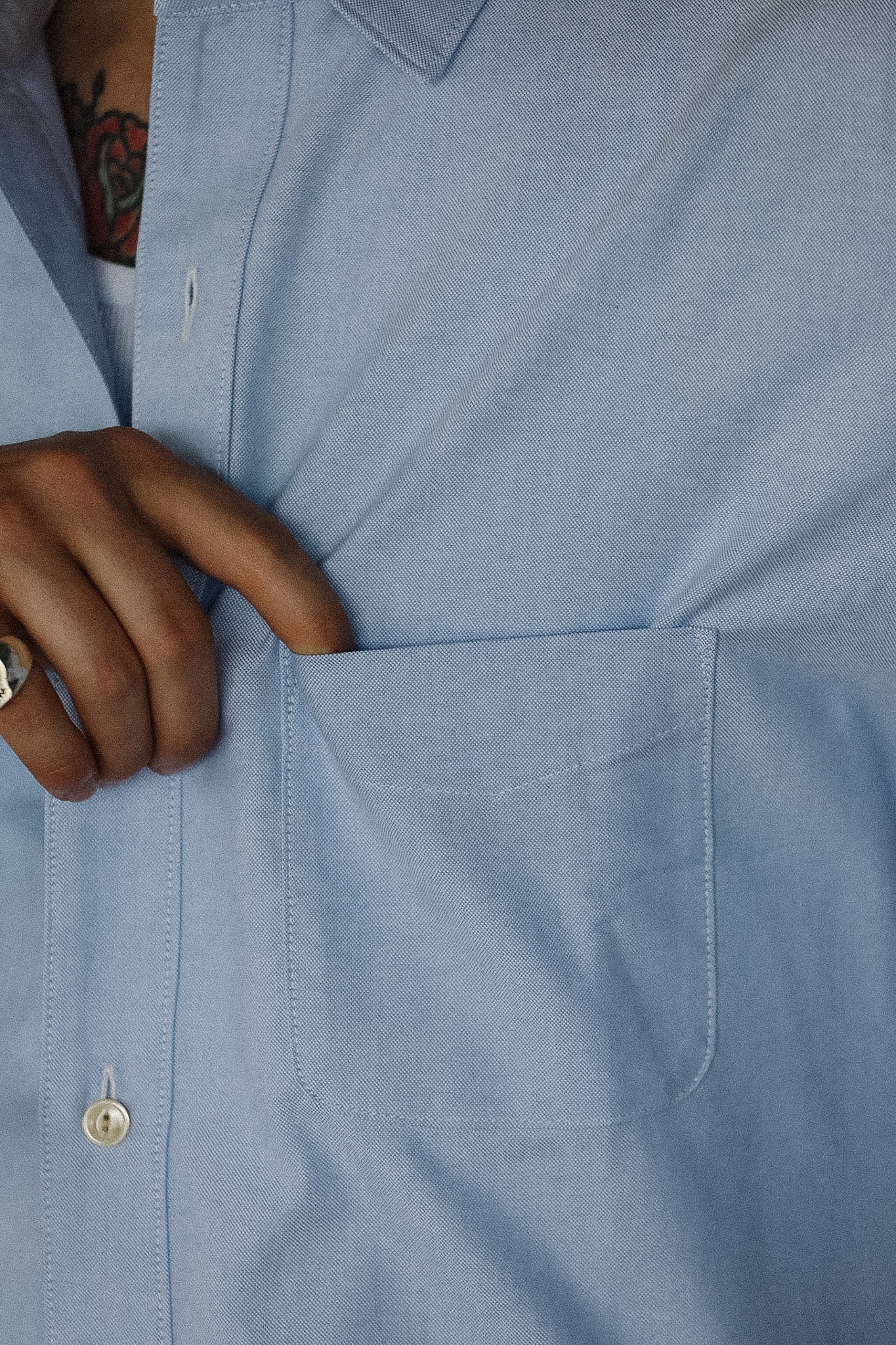 Close-up of a person wearing a light blue shirt with a hand adjusting the collar.