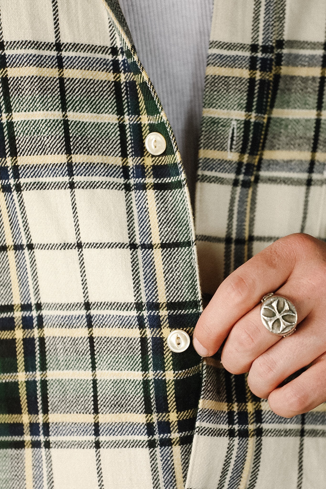 Close-up of a person wearing a plaid jacket with a hand wearing a silver ring.
