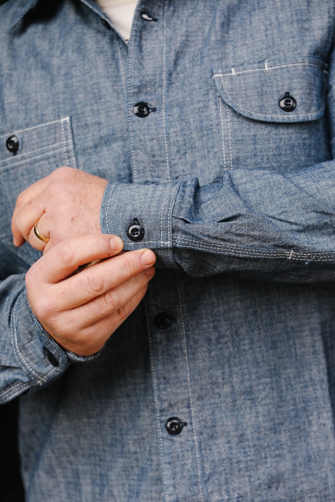 Close-up of man adjusting cuff on blue chambray button-up work shirt with pockets
