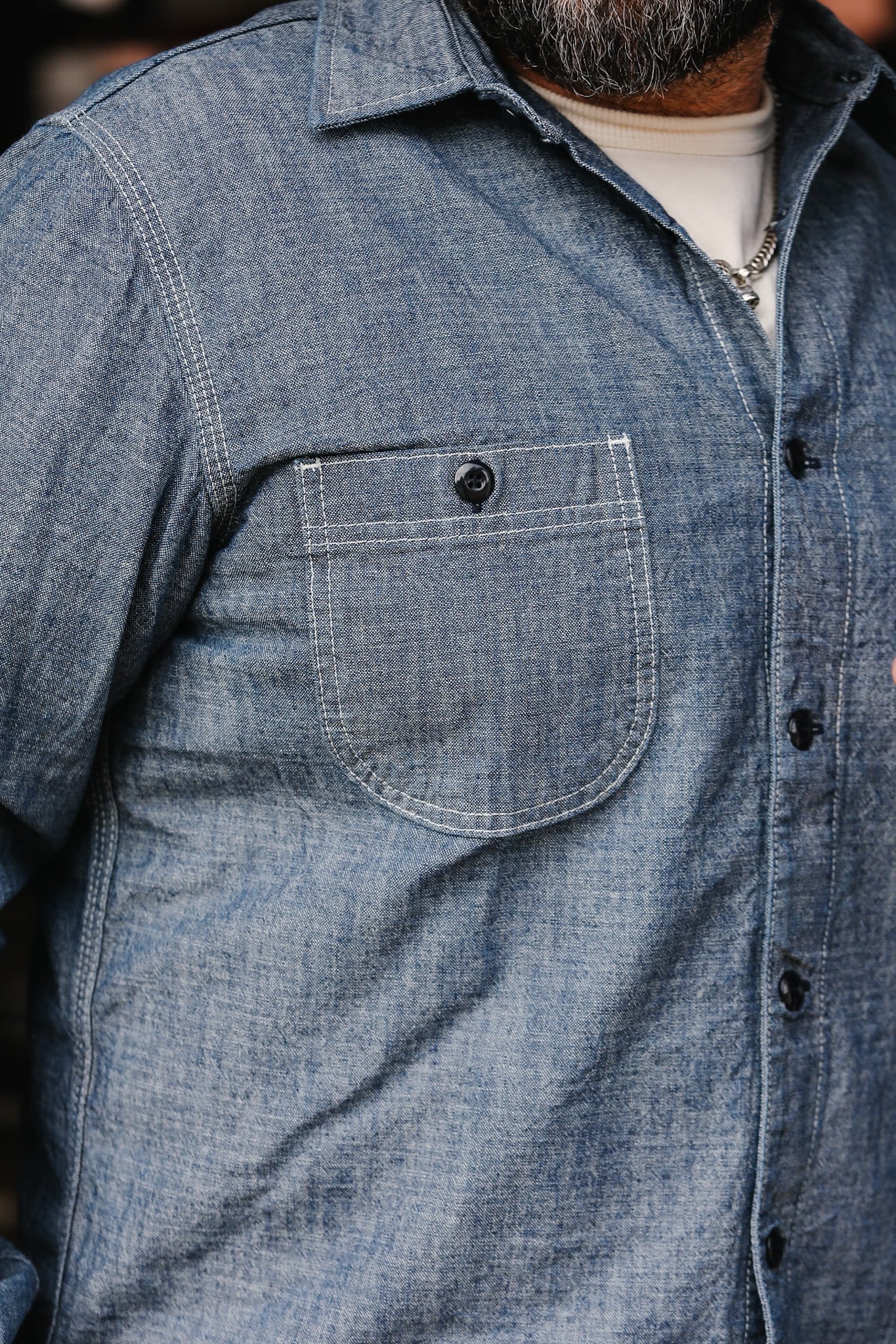 Close-up of man wearing blue denim work shirt with black buttons and chest pocket