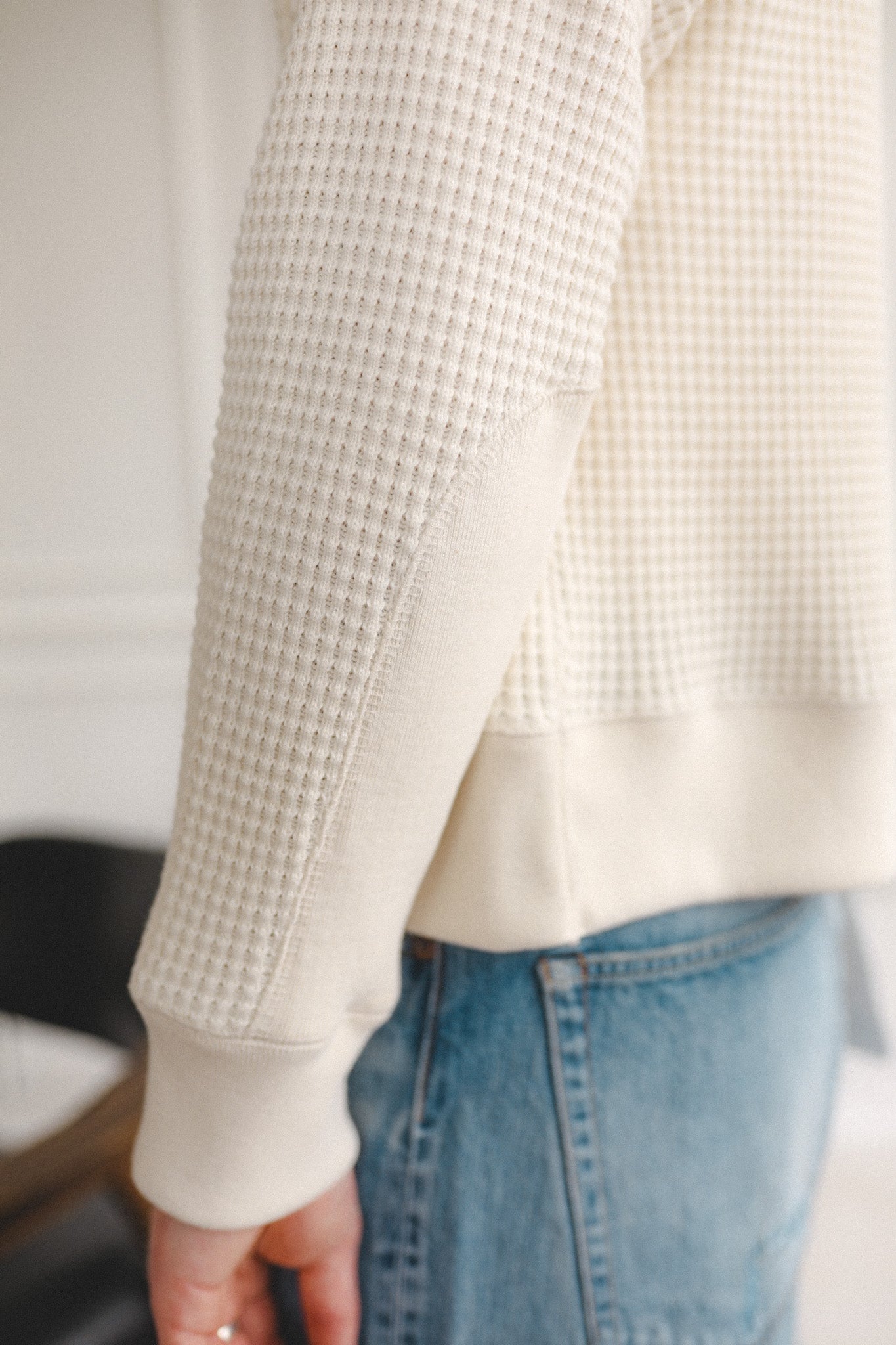 Person wearing a textured beige sweater and blue jeans with a blurred background