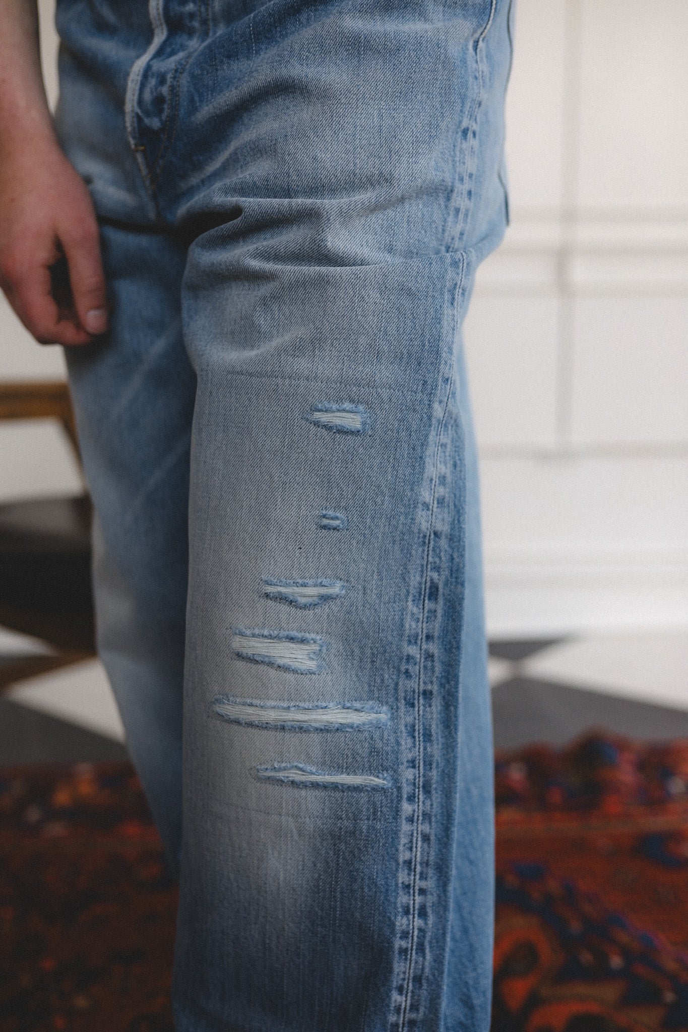 Close-up of a person wearing distressed blue jeans indoors.