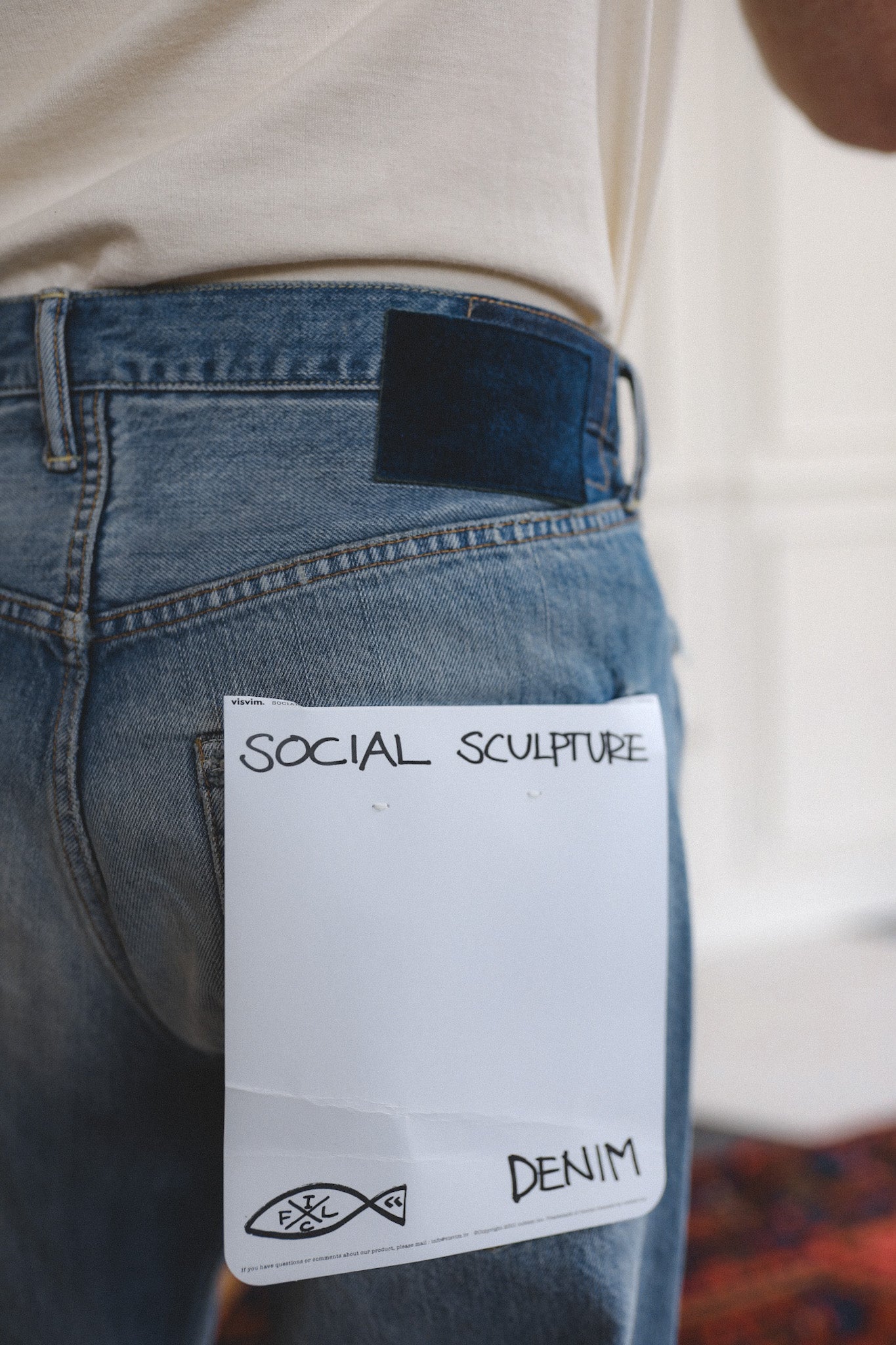 Blue jeans with a label reading 'Social Sculpture Denim' on a blurred background