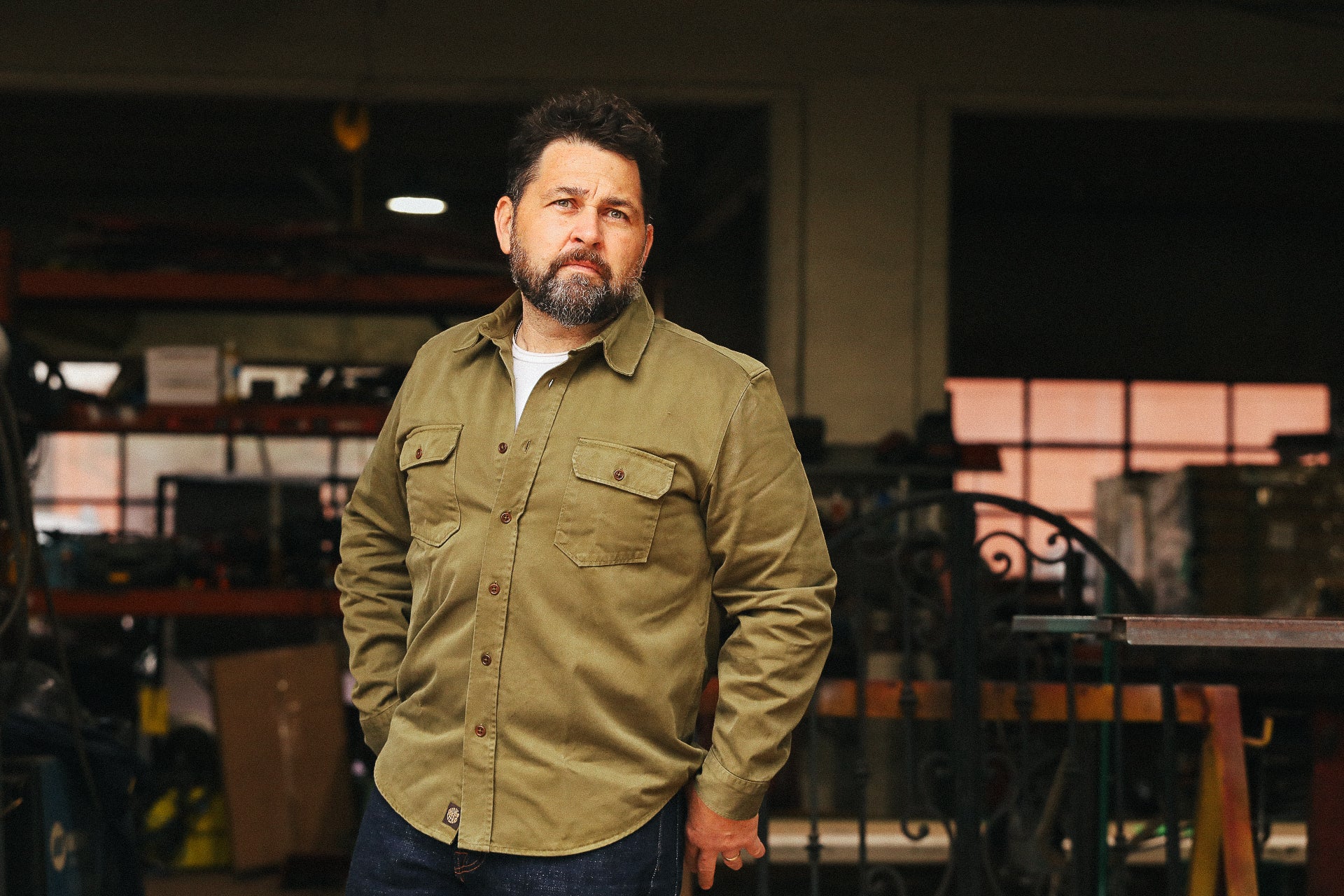 Man wearing a green jacket standing in an indoor setting with shelves and equipment in the background