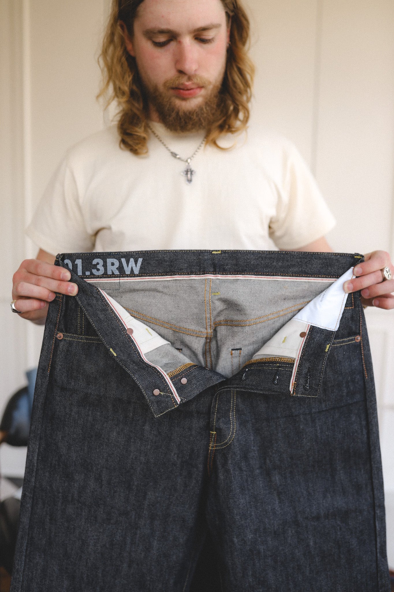 Man holding up a pair of dark blue jeans with visible branding.