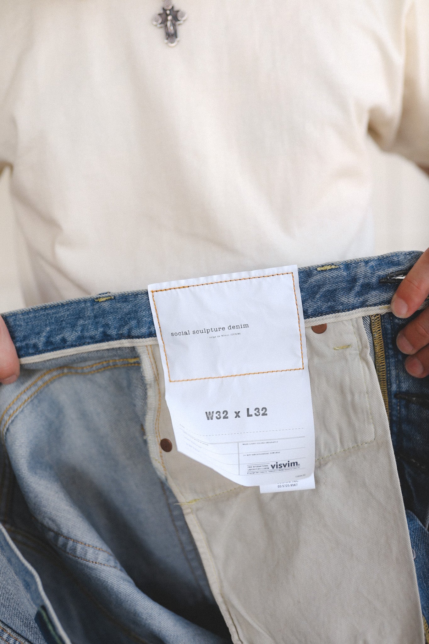 Close-up of a jeans label with a person wearing beige pants and a white shirt.