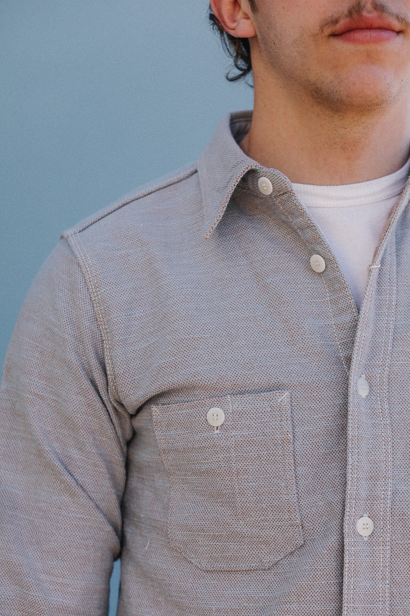 Close-up of a person wearing a gray button-up shirt against a blue background