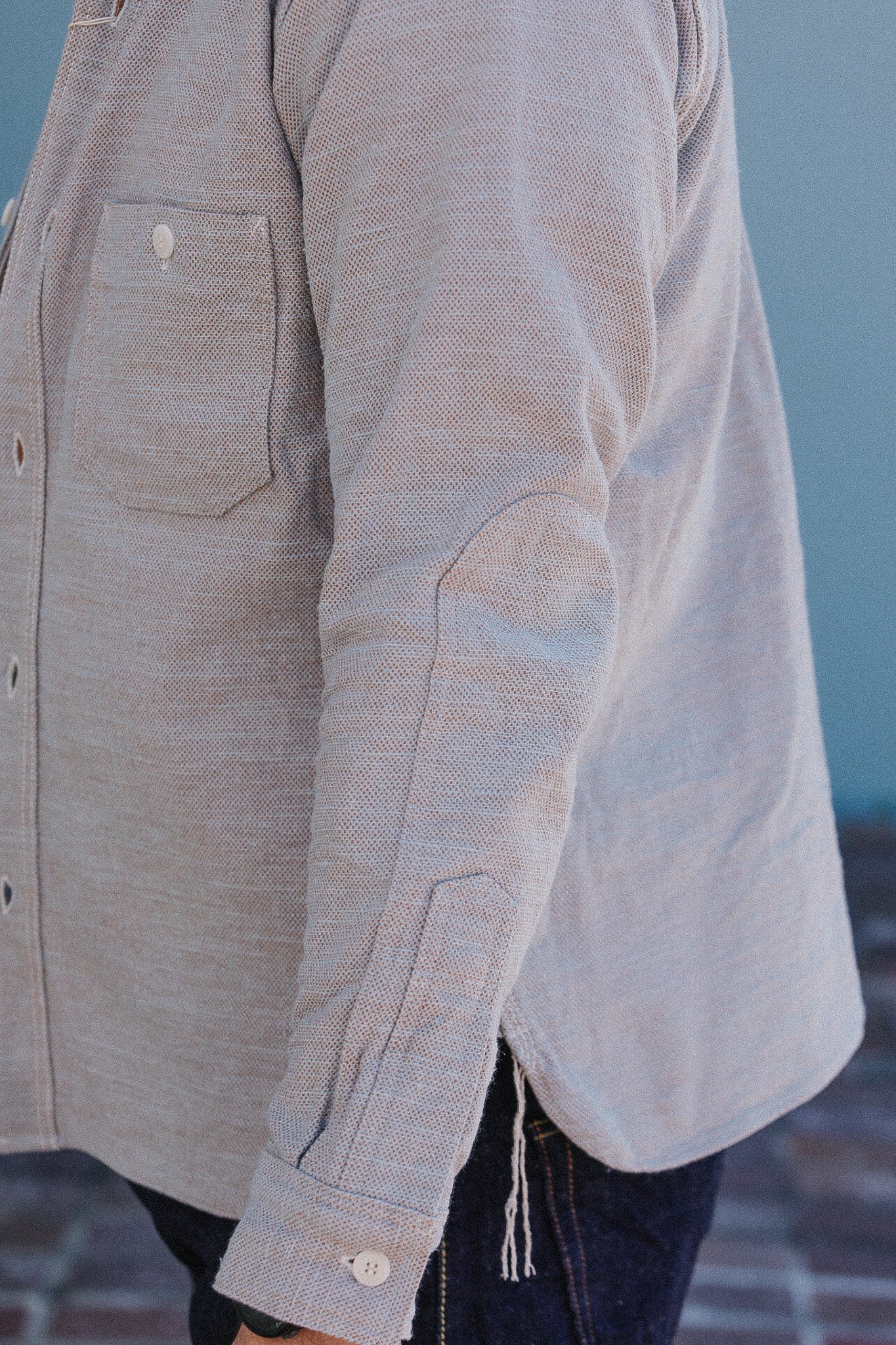 Close-up of a person wearing a light brown button-up shirt with a blurred background