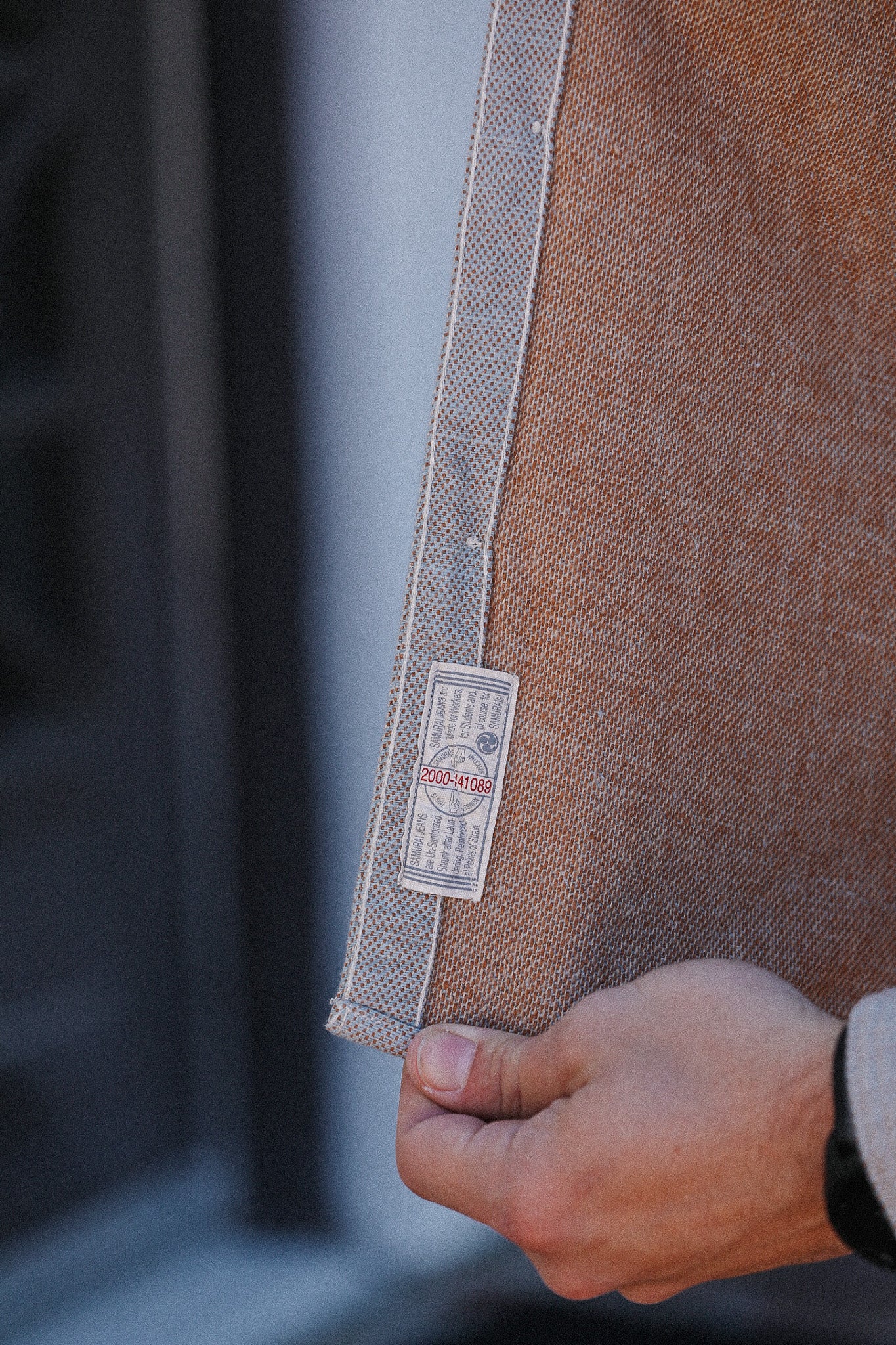 Close-up of a brown fabric with a label held by a hand against a blurred background