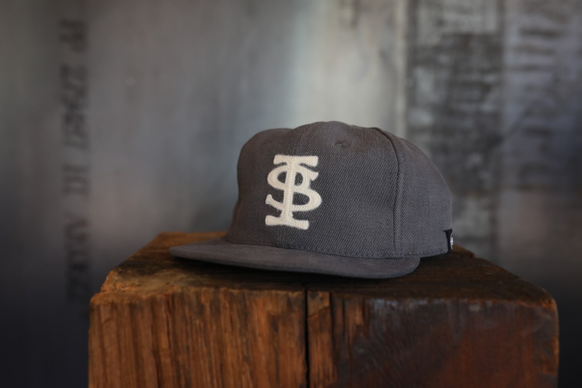 Gray cap with a logo on a wooden block against a textured wall.