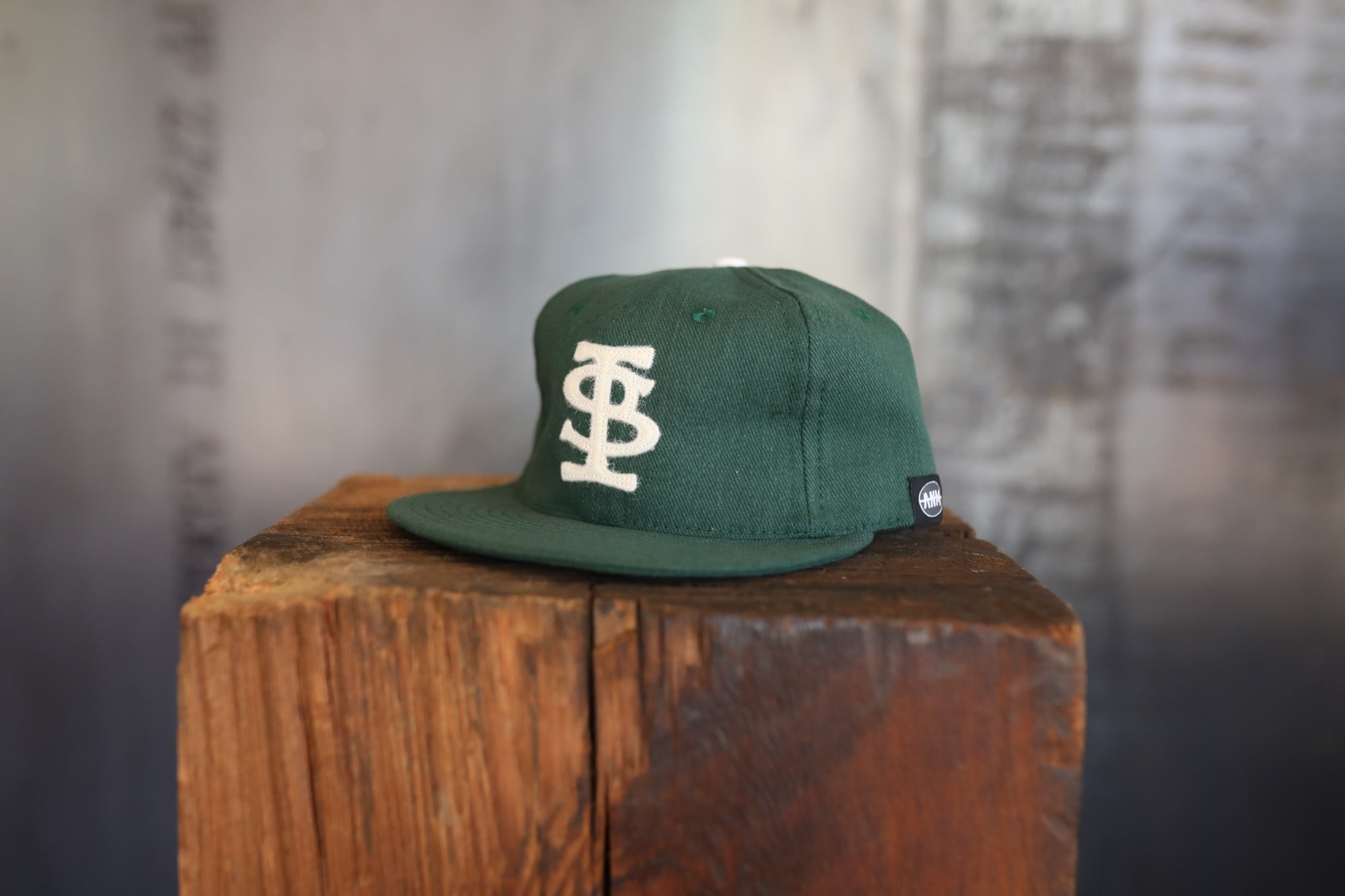 Green cap with white logo on a wooden block against a textured wall.