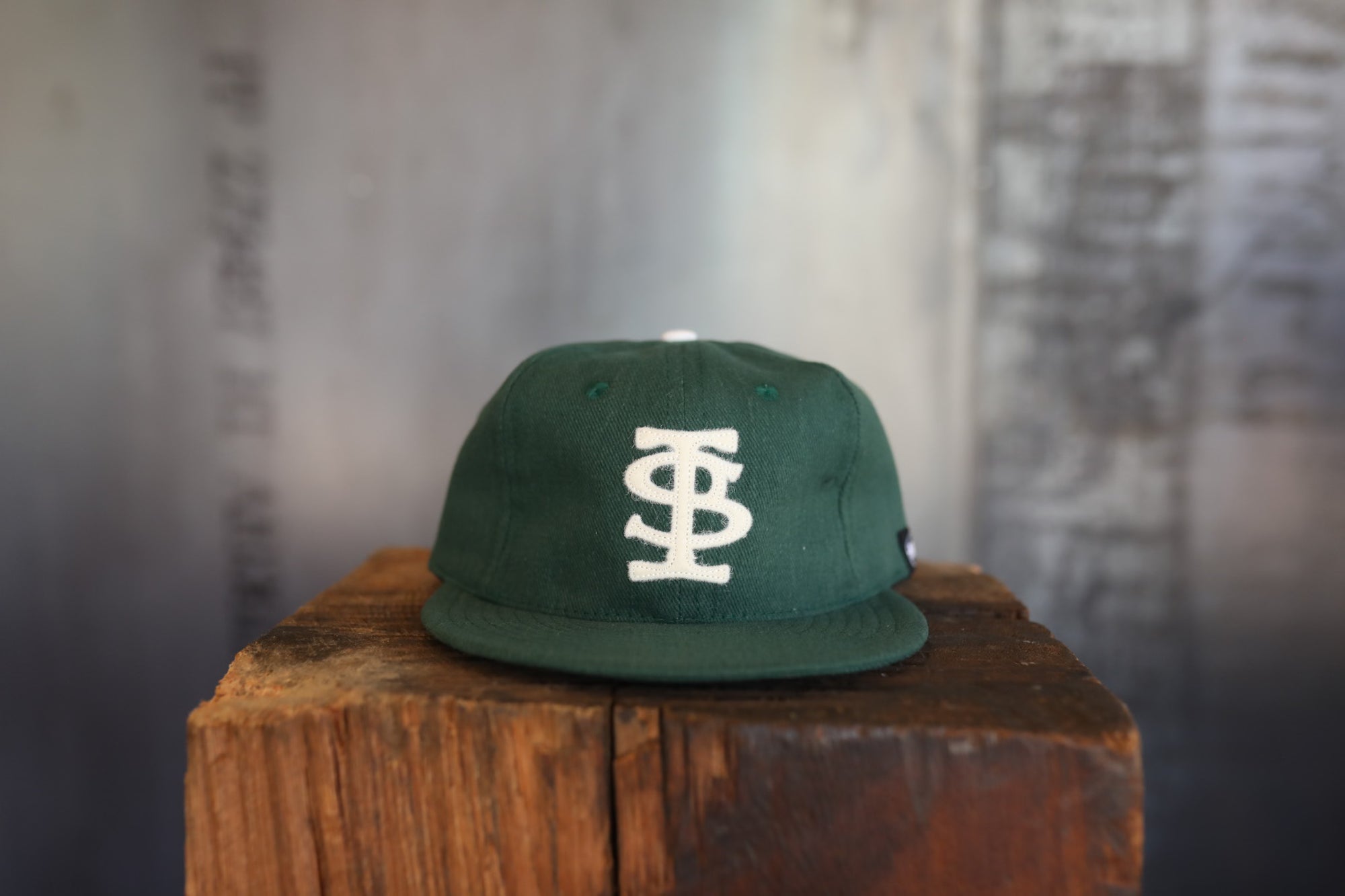 Green cap with a logo on a wooden block against a textured wall.