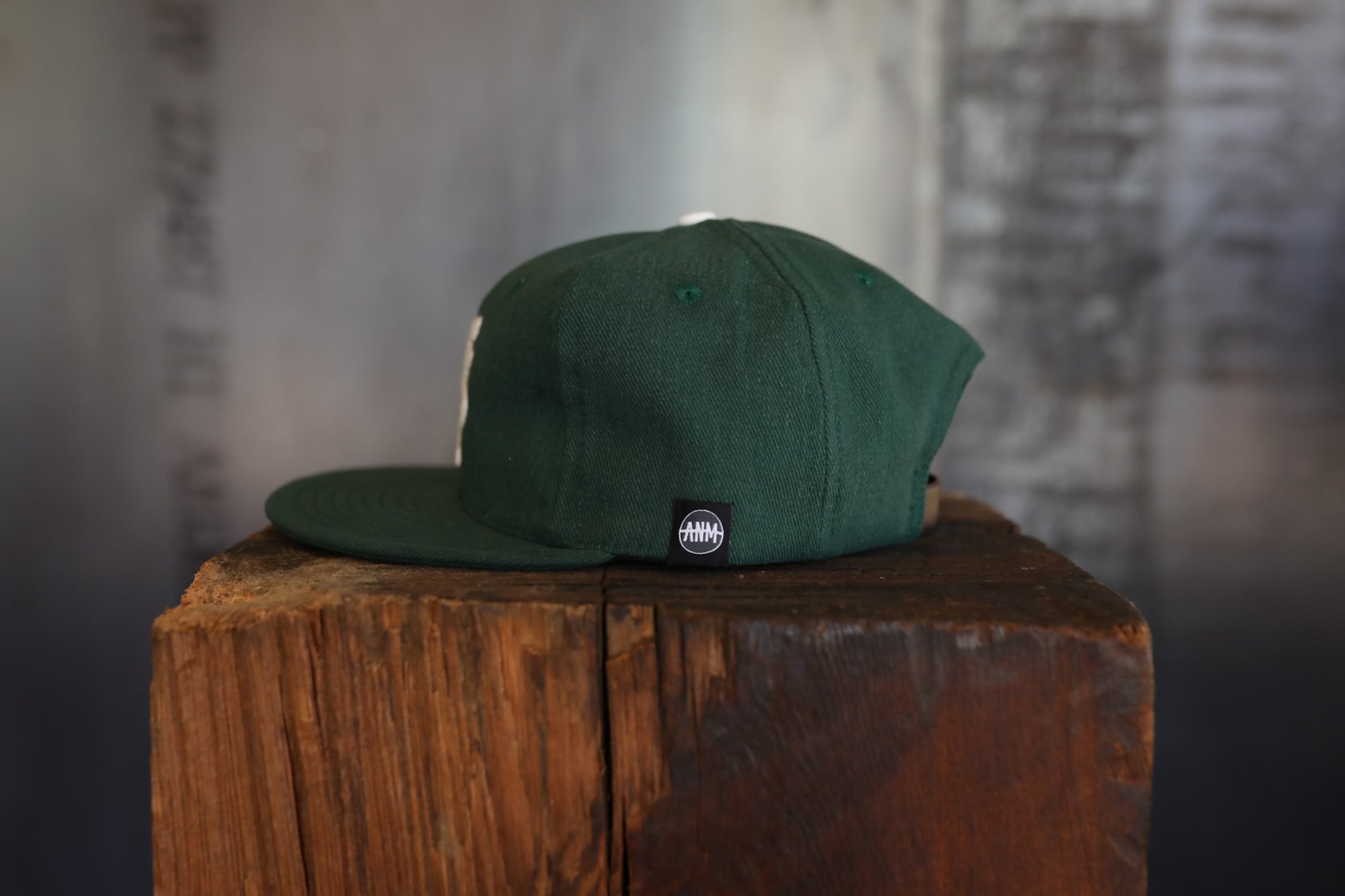 Green cap with a logo on a wooden block against a textured wall.