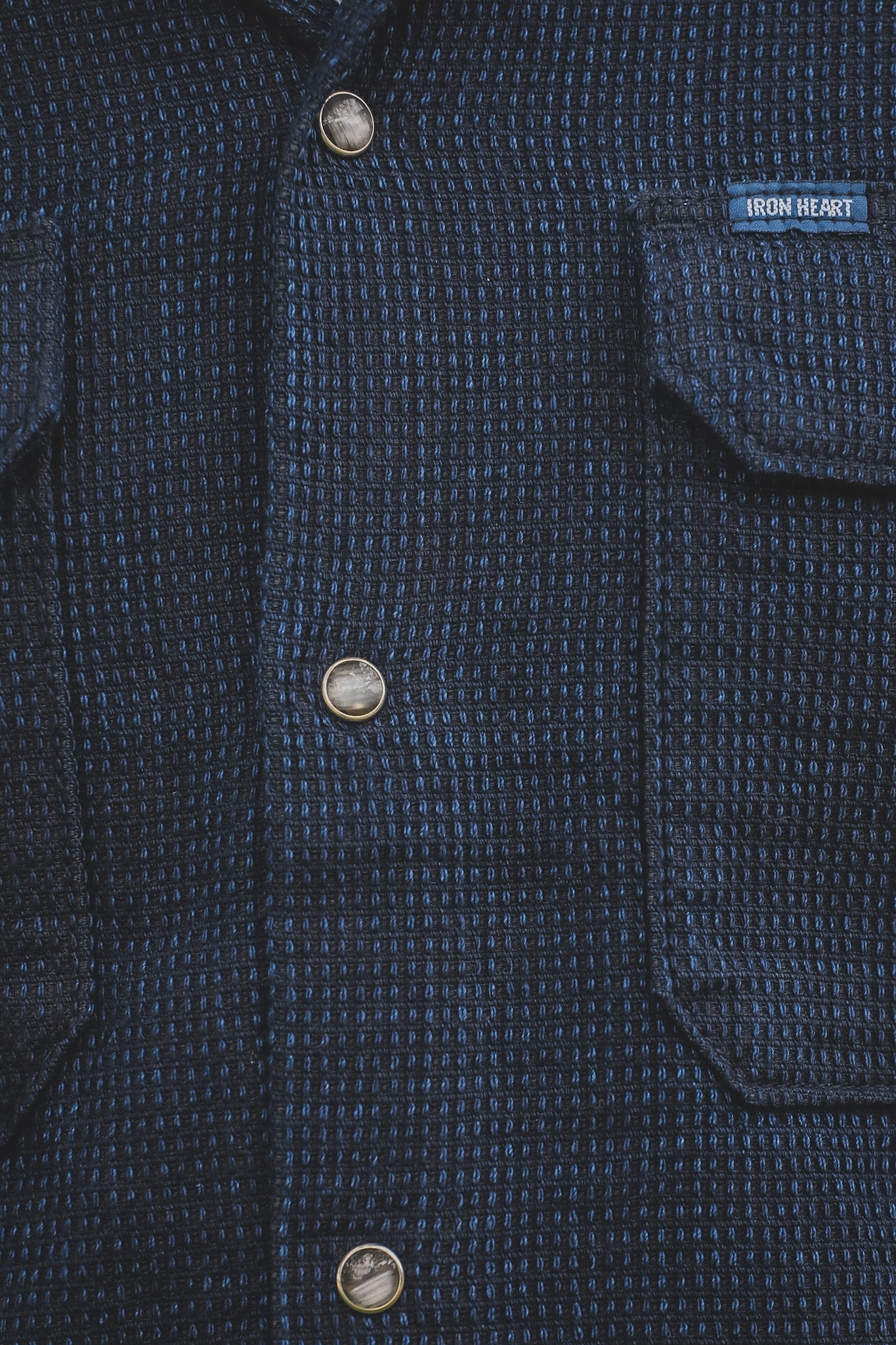 Close-up of a dark blue textured shirt with button details and 'Iron Heart' brand label.