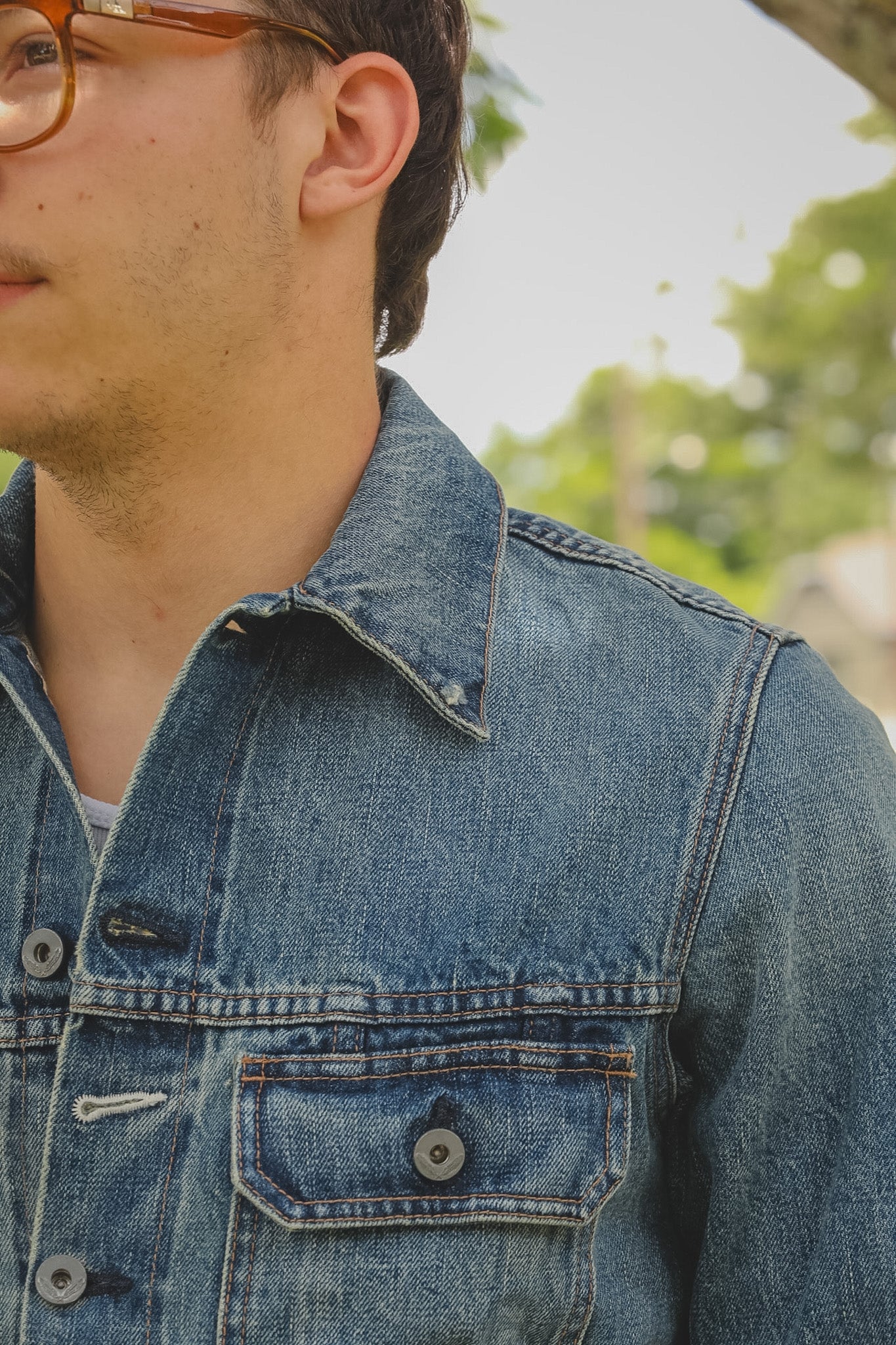 Close-up of a person wearing a blue denim jacket with a blurred outdoor background