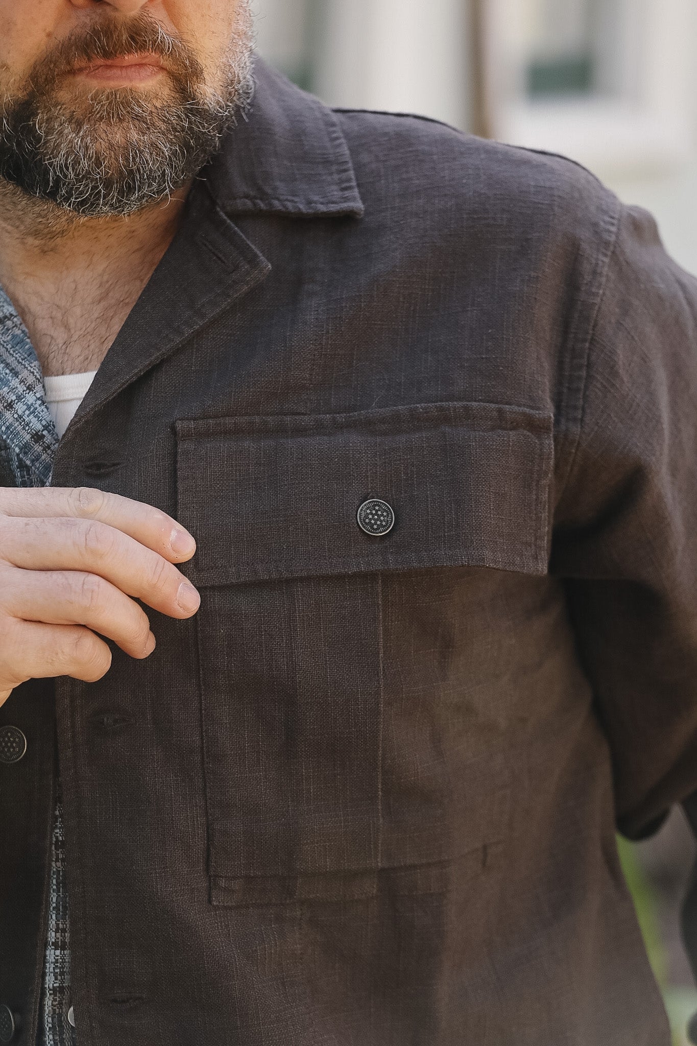 Man wearing a dark brown jacket with a button, blurred background