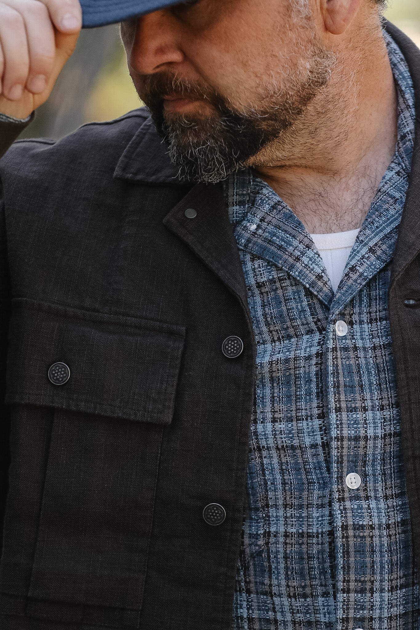 Man wearing a black coat over a plaid shirt with a blue cap.