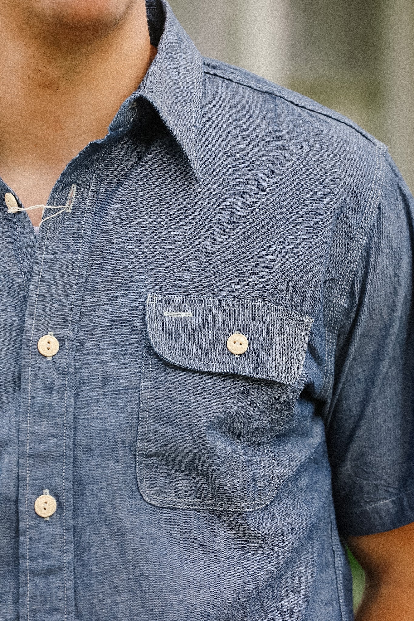 Close-up of a person wearing a blue short-sleeve shirt with a pocket and buttons.