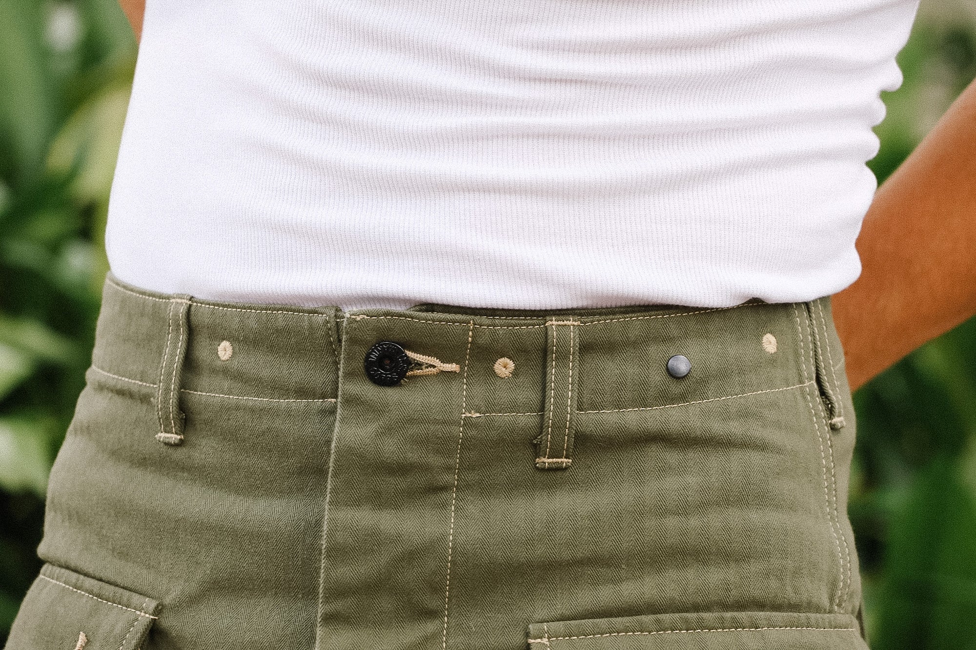 Person wearing green pants with a white shirt against a blurred natural background