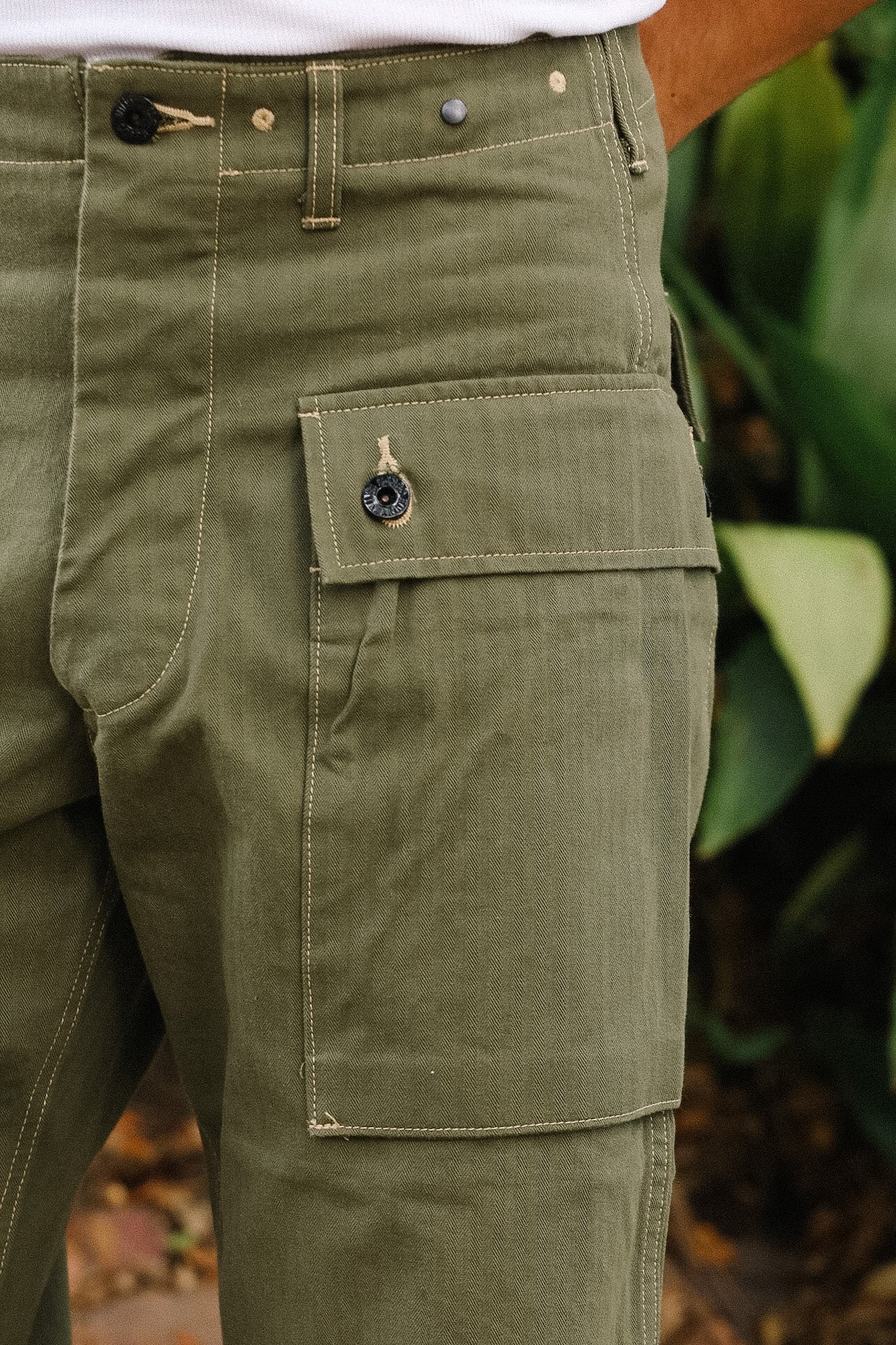 Close-up of green pants with a pocket detail, blurred natural background