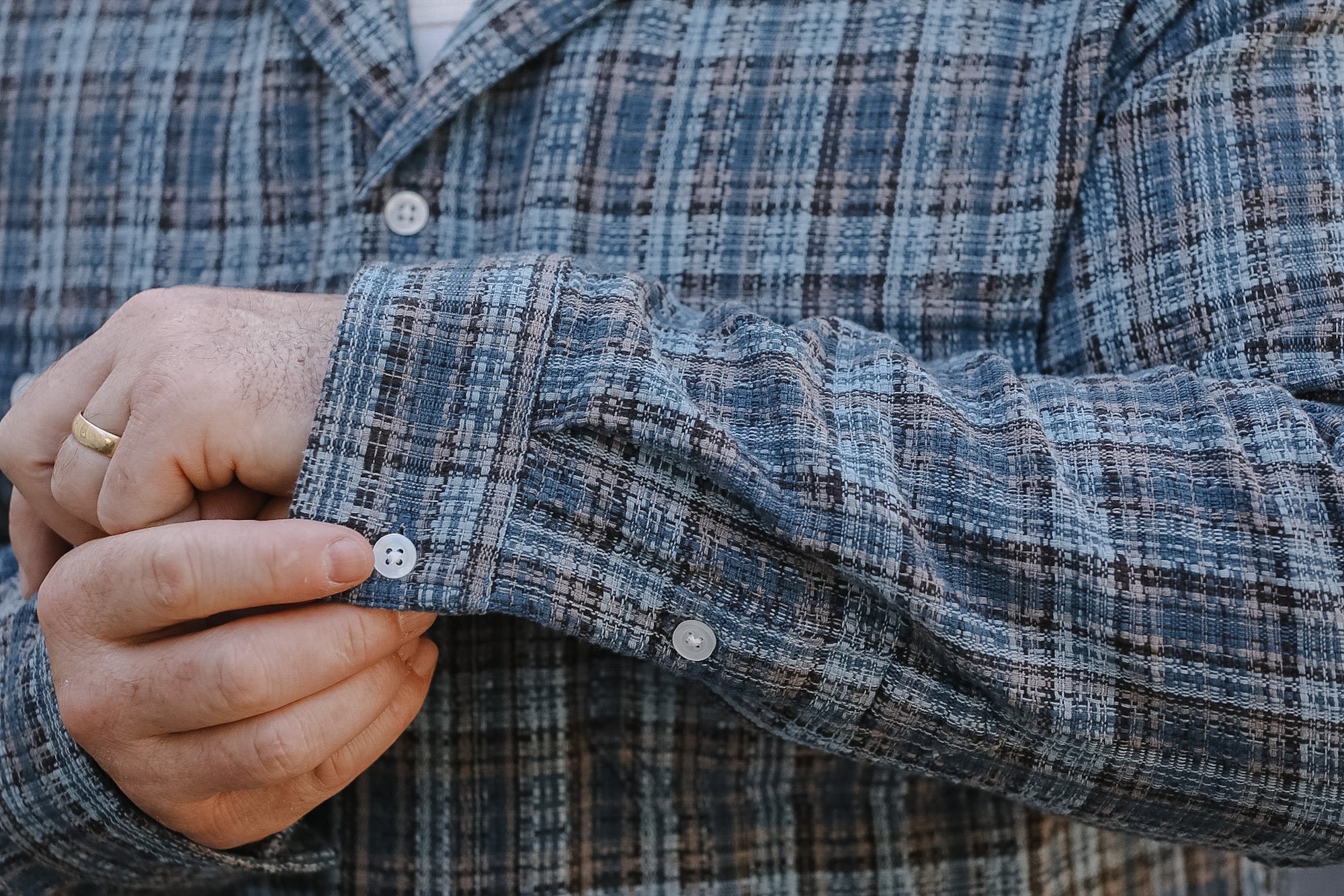 Close-up of a person wearing a plaid shirt with a focus on the sleeve and hand.