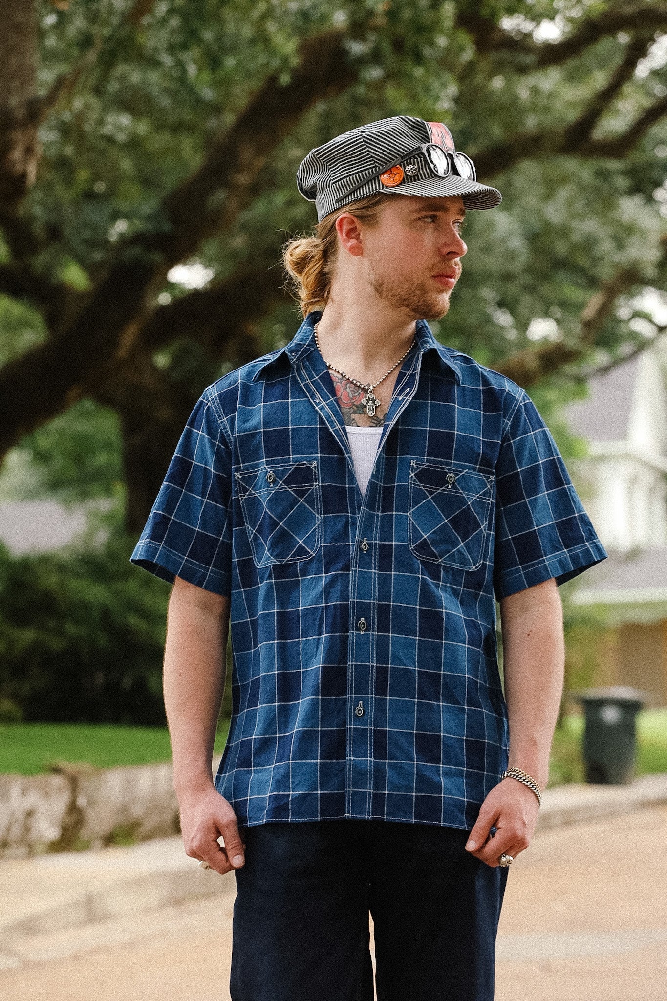 Man wearing a blue plaid shirt and cap outdoors with trees in the background