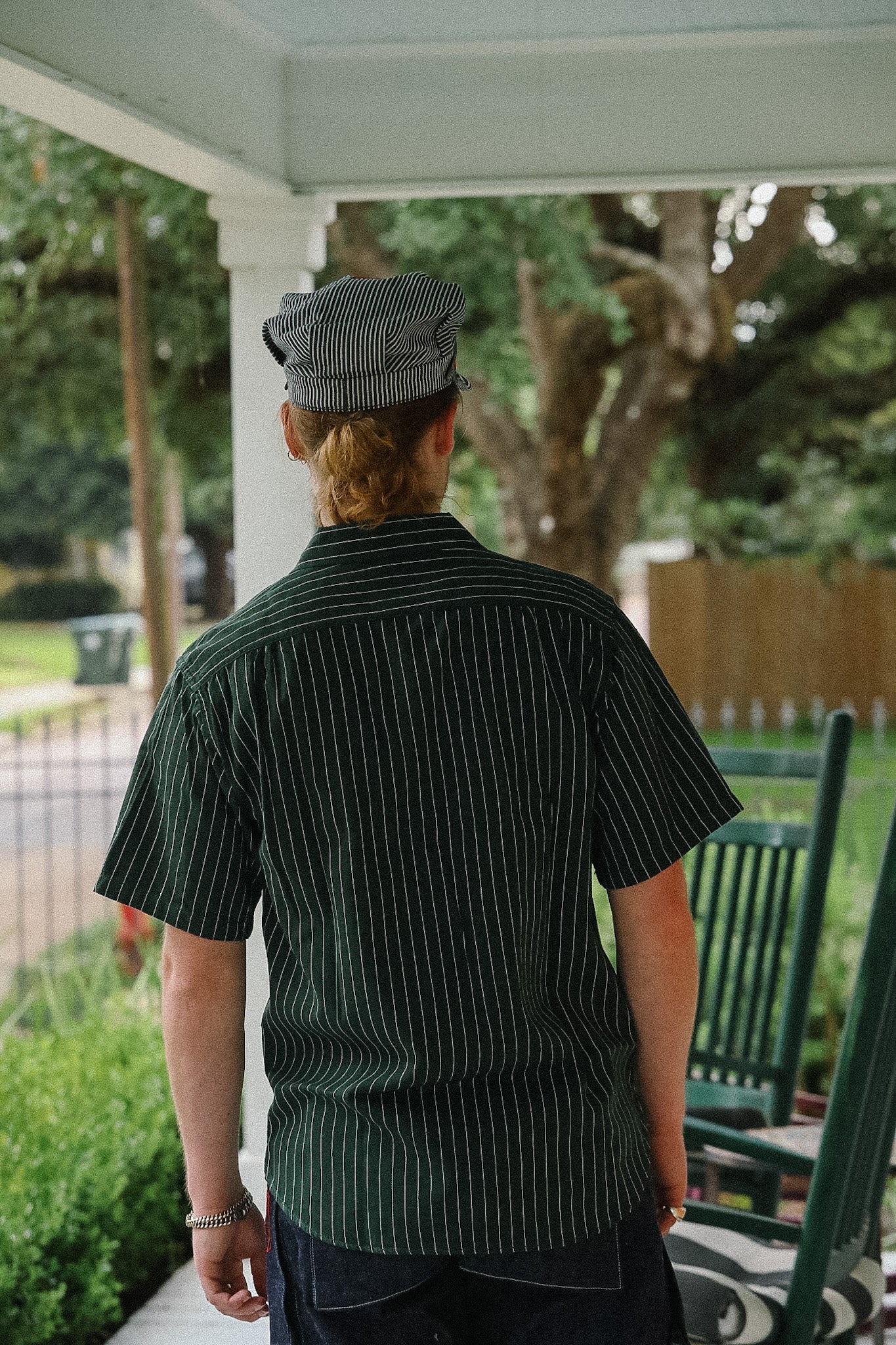 Person wearing a green striped shirt and cap on a porch