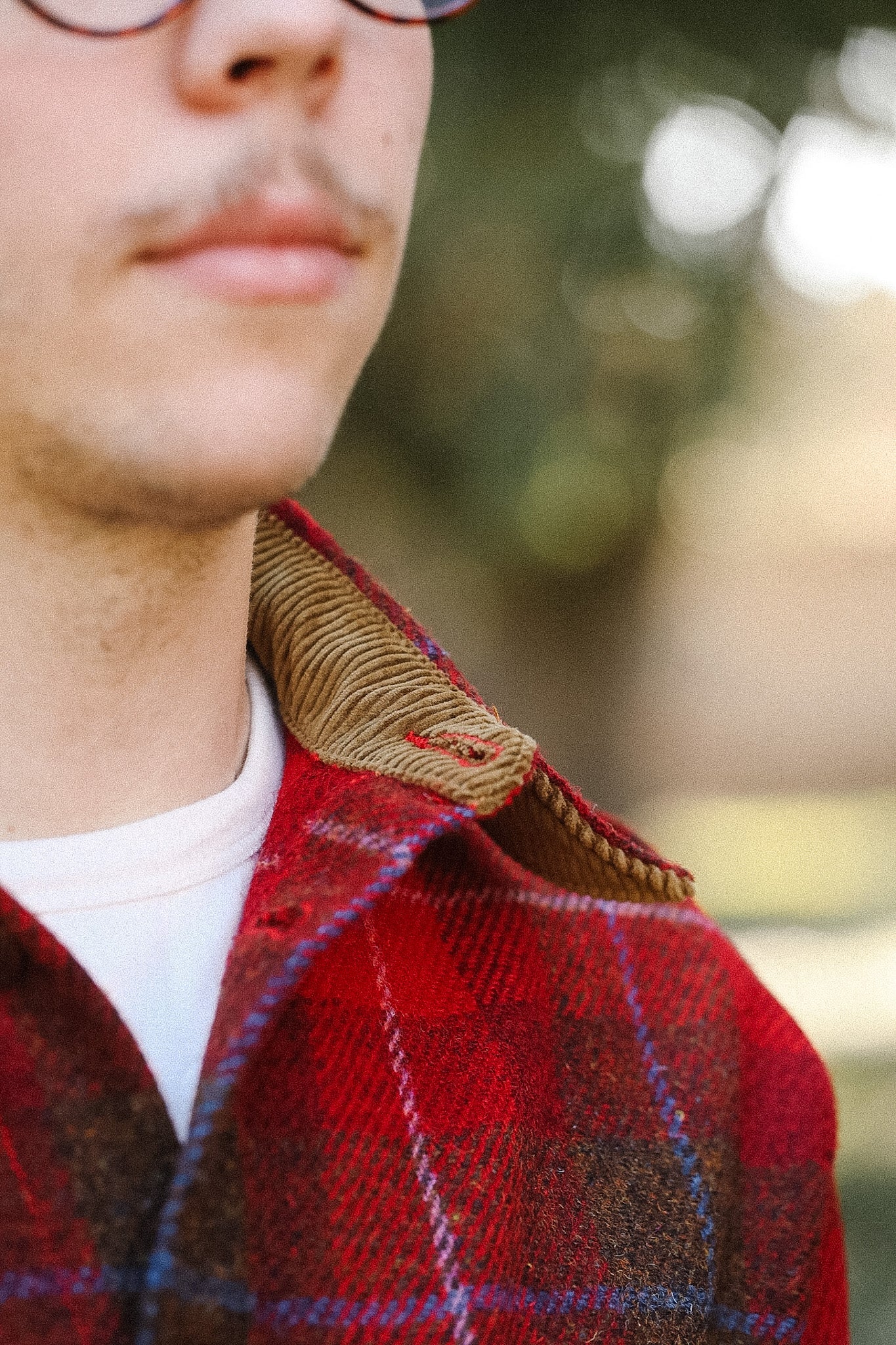 Close-up of a person wearing a red plaid jacket with a blurred outdoor background
