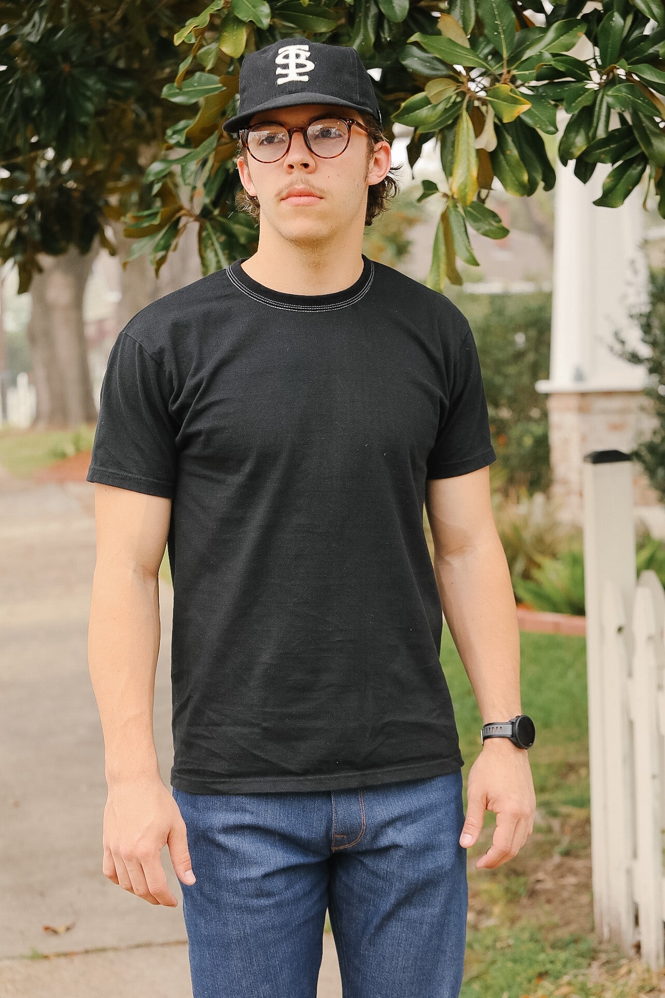 Person wearing a black t-shirt and cap outdoors with greenery in the background