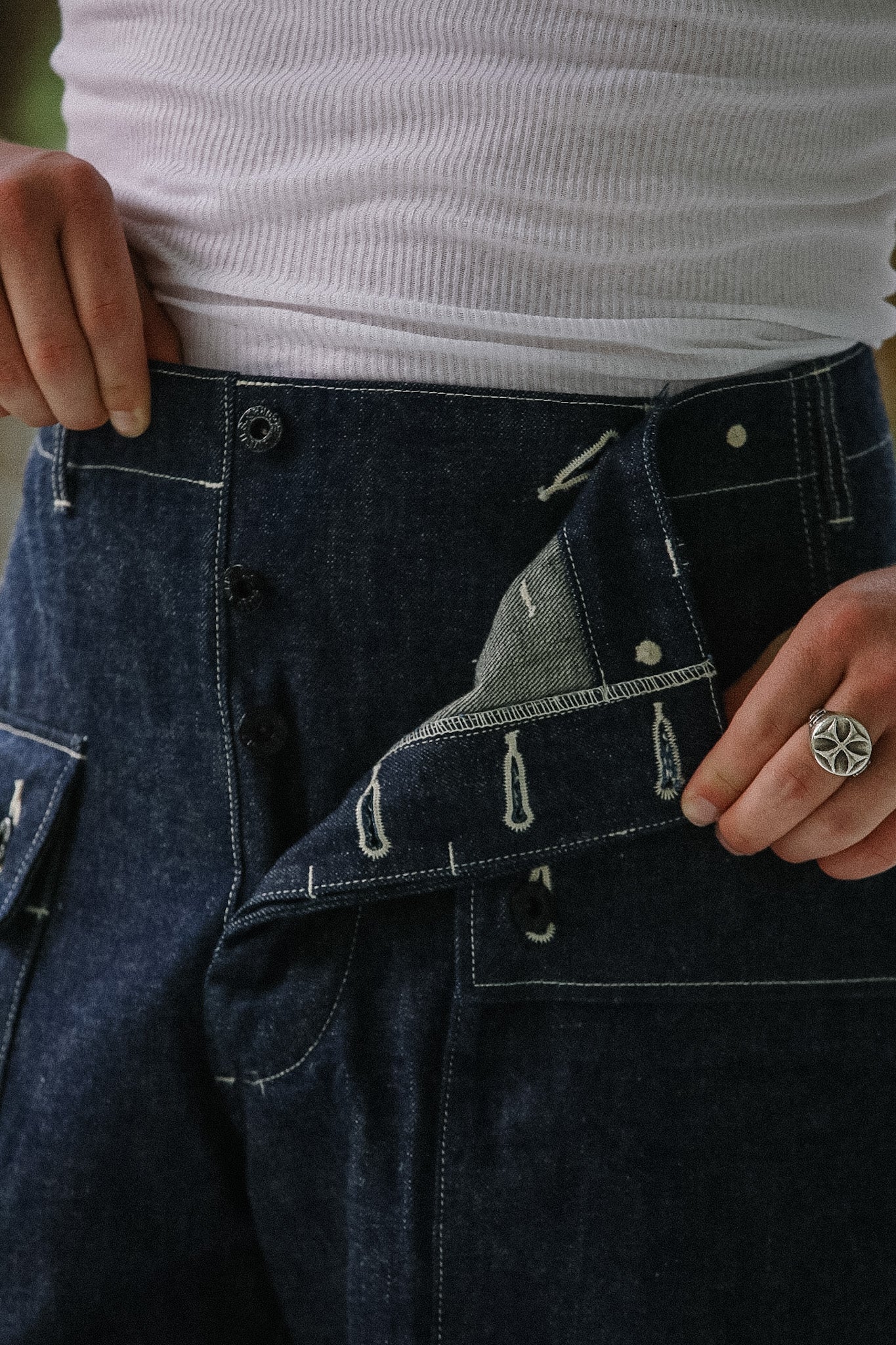 Close-up of a person wearing dark blue jeans with a white shirt underneath.