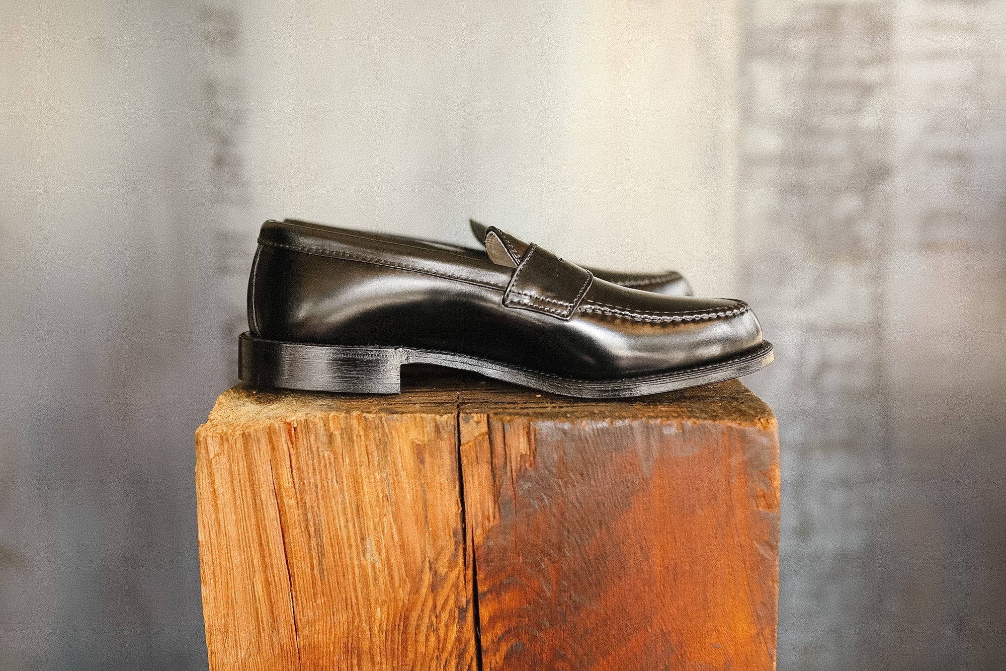 Pair of black leather loafers on a wooden block with a neutral background