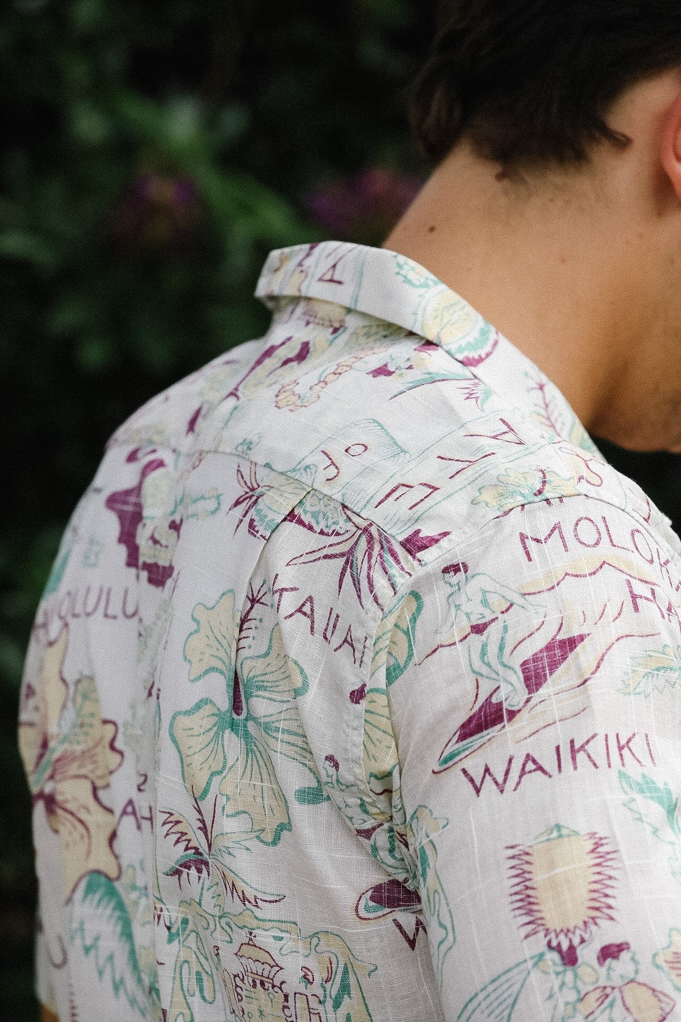 Person wearing a colorful floral shirt with text, standing against a blurred natural background.