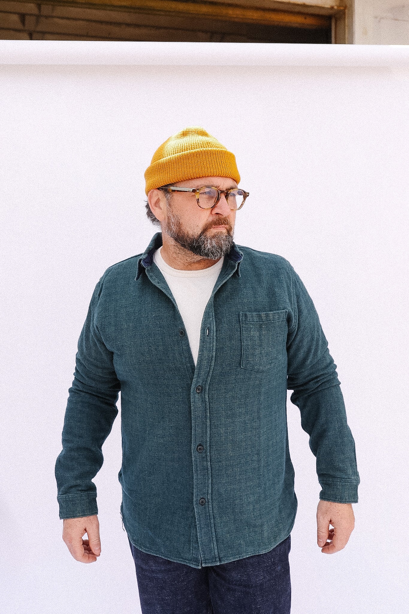 Man wearing a green shirt, white t-shirt, and yellow beanie against a white background