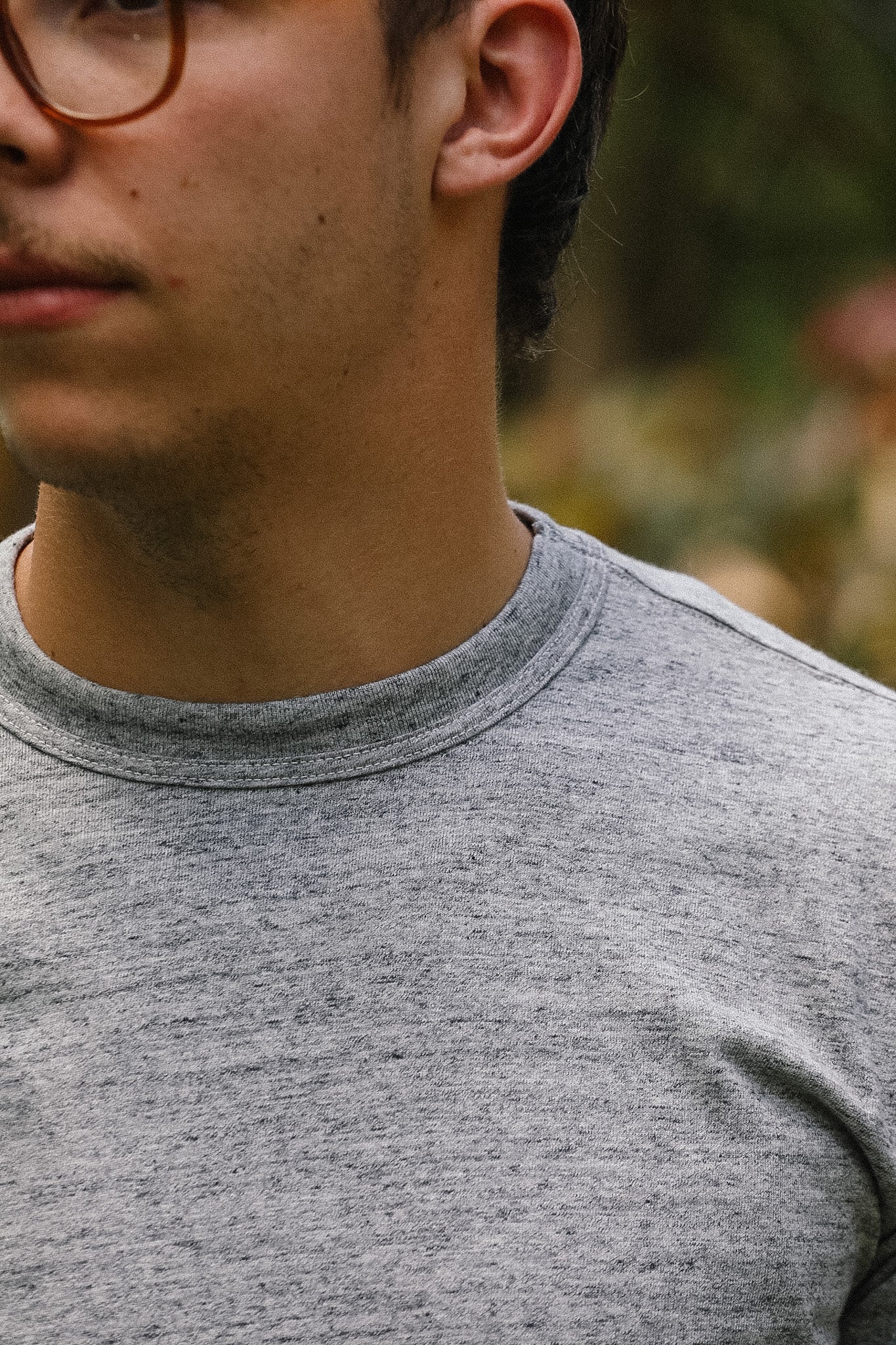 Close-up of a person wearing a gray shirt with a blurred natural background