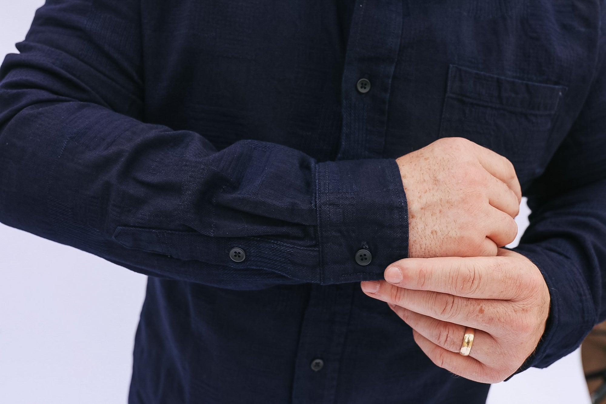 Person wearing a navy blue shirt with rolled-up sleeves, holding hands together.