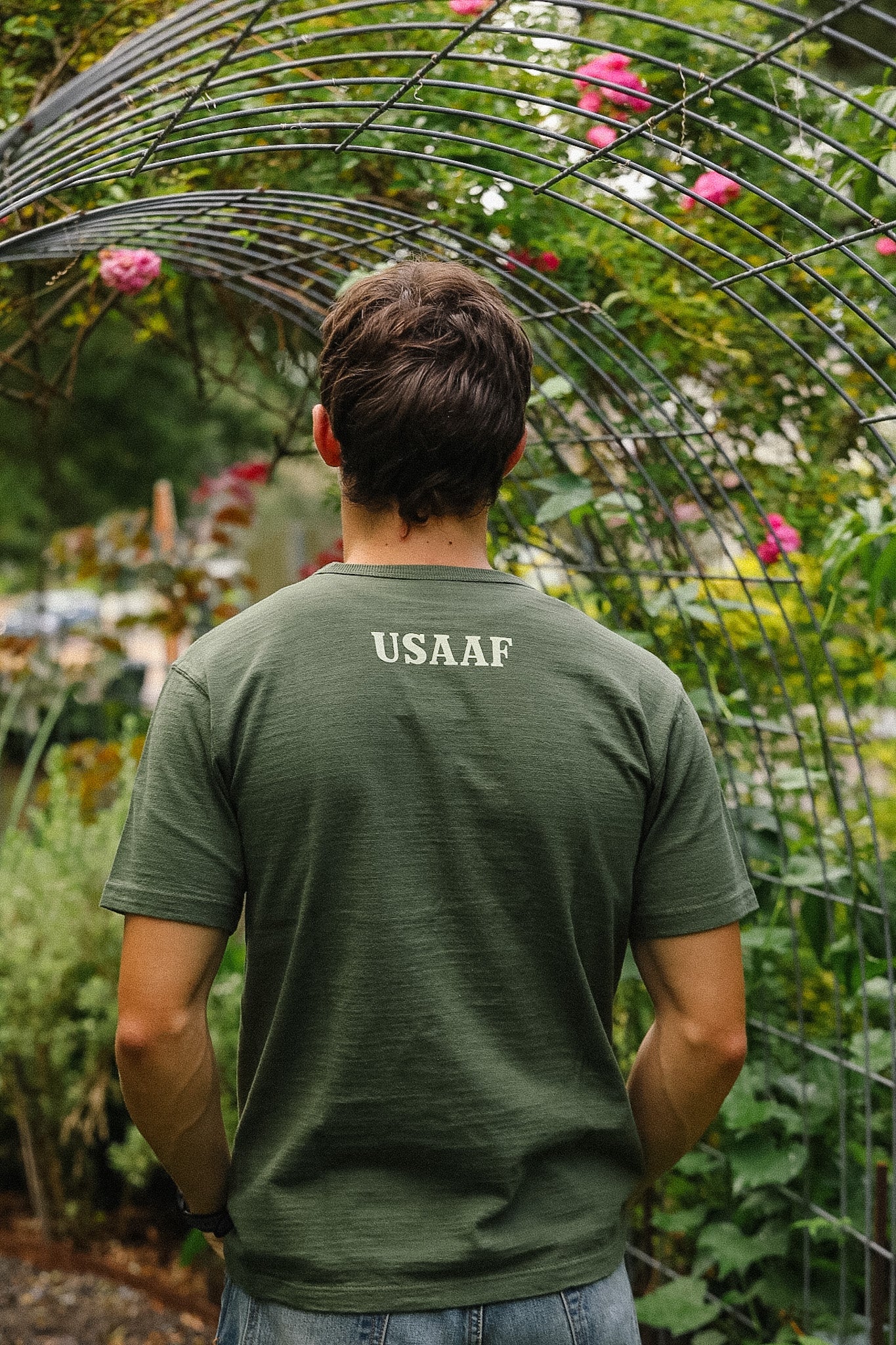 Person wearing a green USAAF t-shirt standing in a garden with plants and flowers.