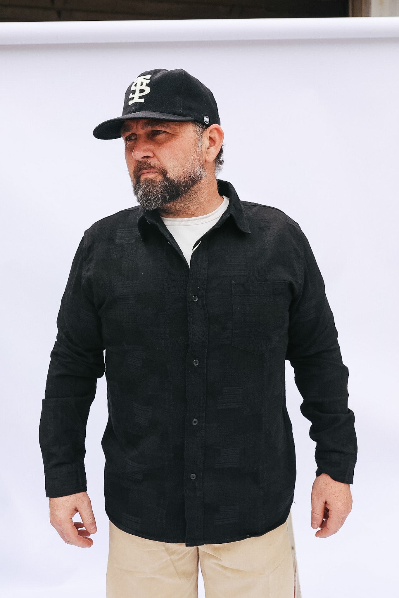 Man wearing a black shirt and cap with a logo against a white background