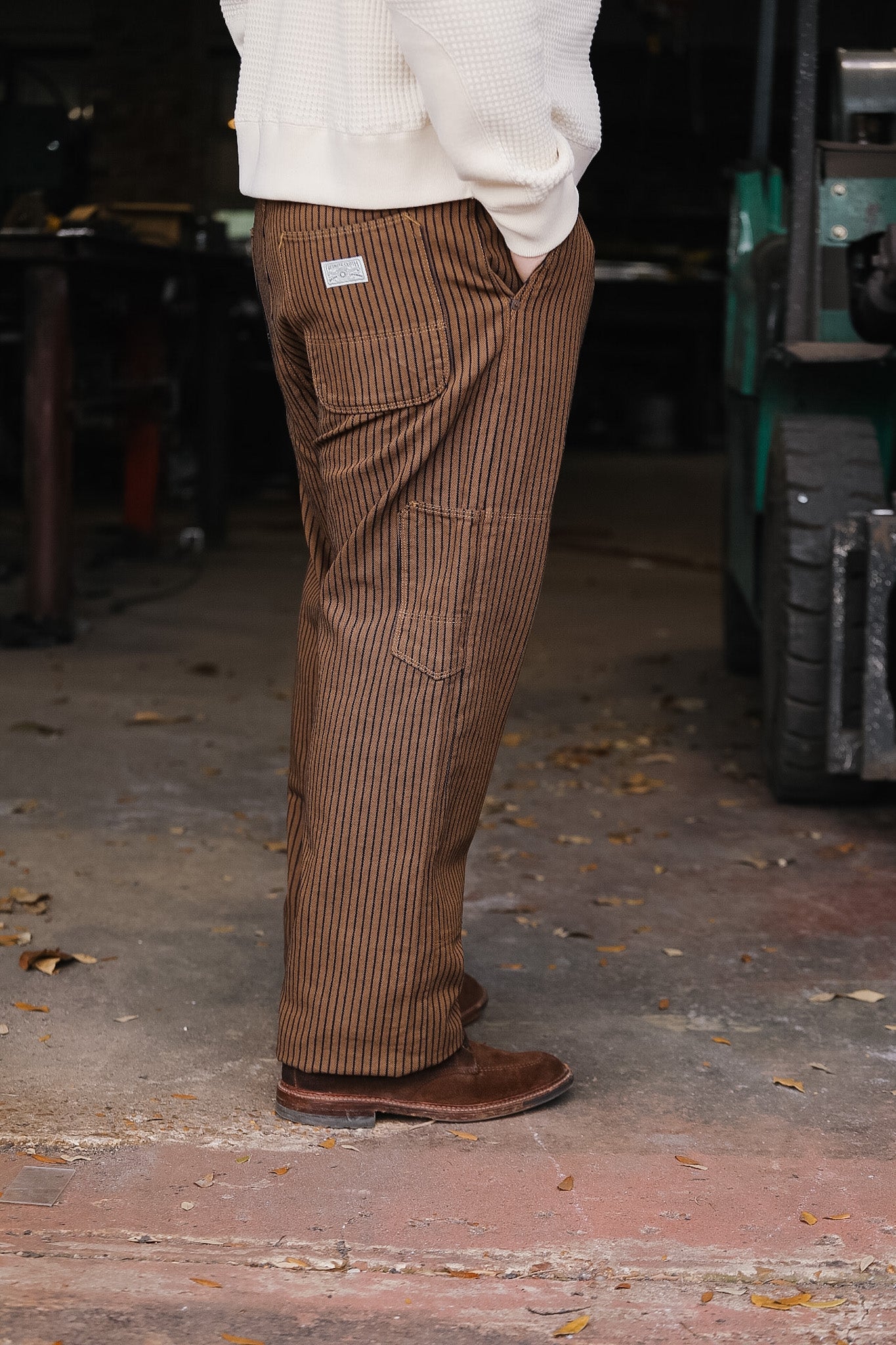 Person wearing brown striped pants and a white sweater in an indoor setting.
