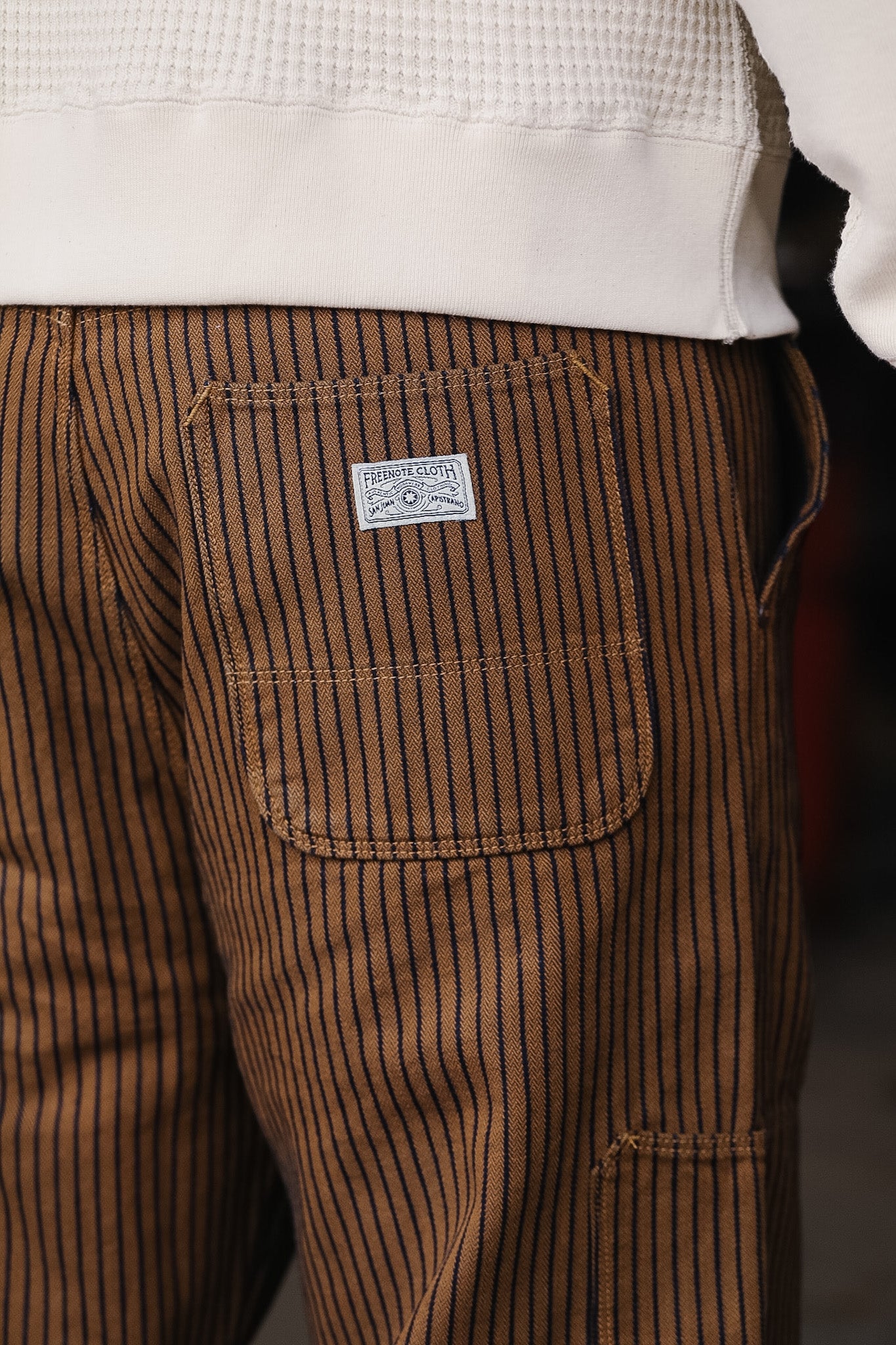 Brown striped pants with a brand label on the pocket against a blurred background
