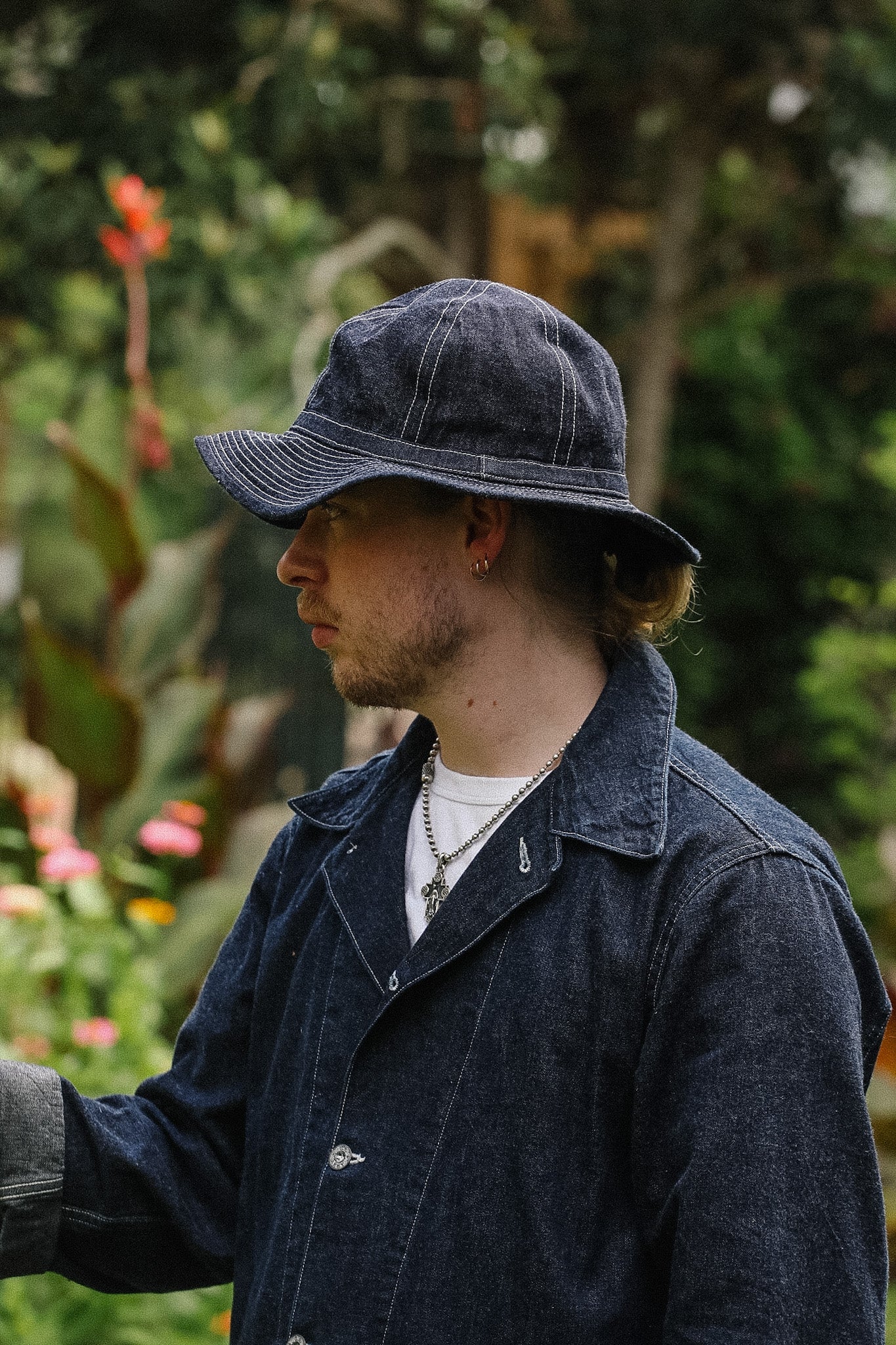 Person wearing a denim hat and coat in a garden setting