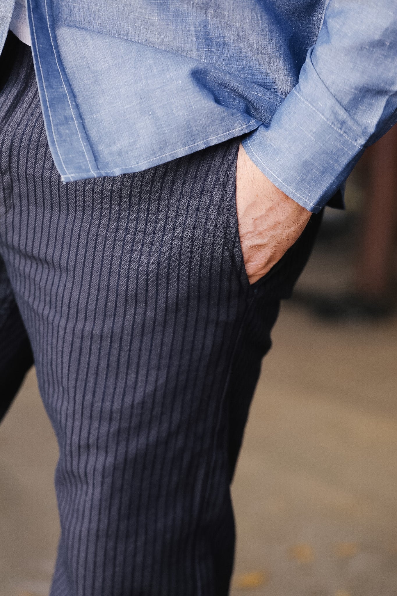 Person wearing a blue shirt and dark pinstripe pants with one hand in their pocket.