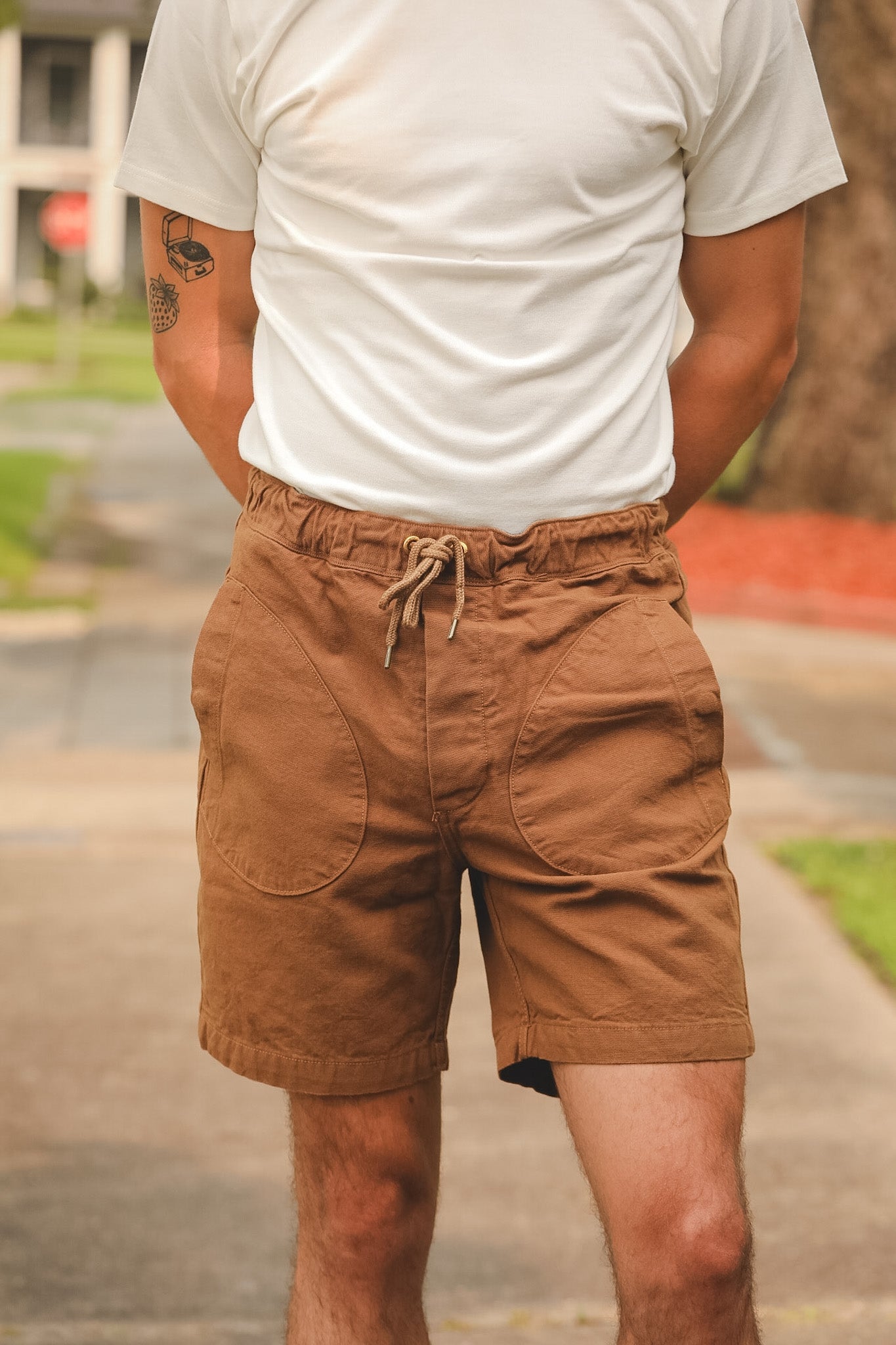 Person wearing brown shorts and a white t-shirt with a blurred outdoor background