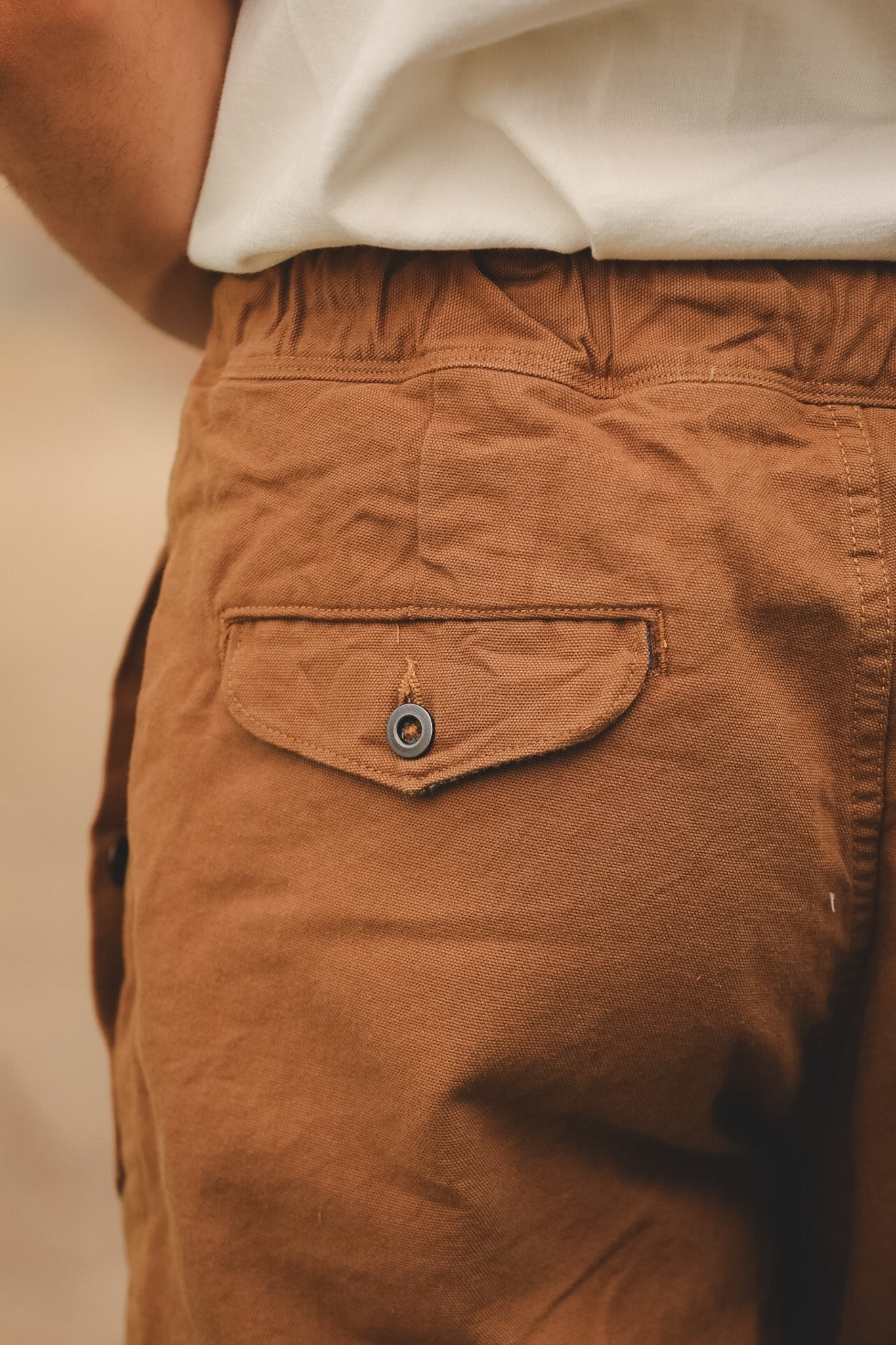 Close-up of brown pants with a pocket and button on a neutral background