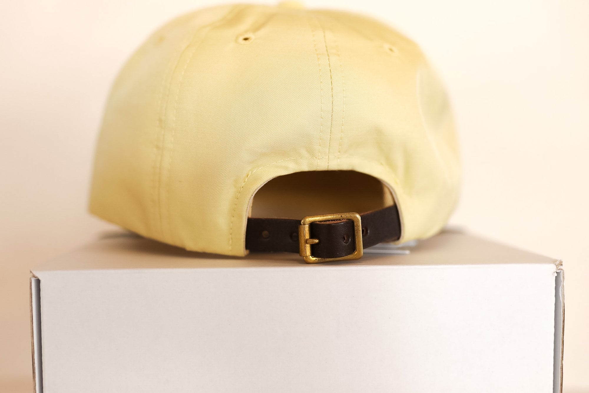 Yellow cap with a black buckle on a white box against a beige background